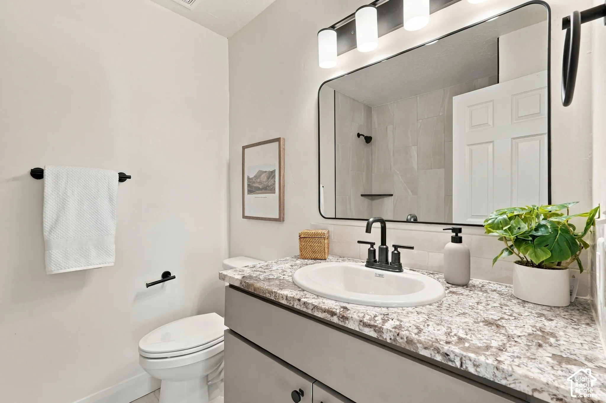 Bathroom featuring a vanity with a stone-patterned countertop, an undermount sink, a three-light fixture, a rectangular mirror, and matte black hardware