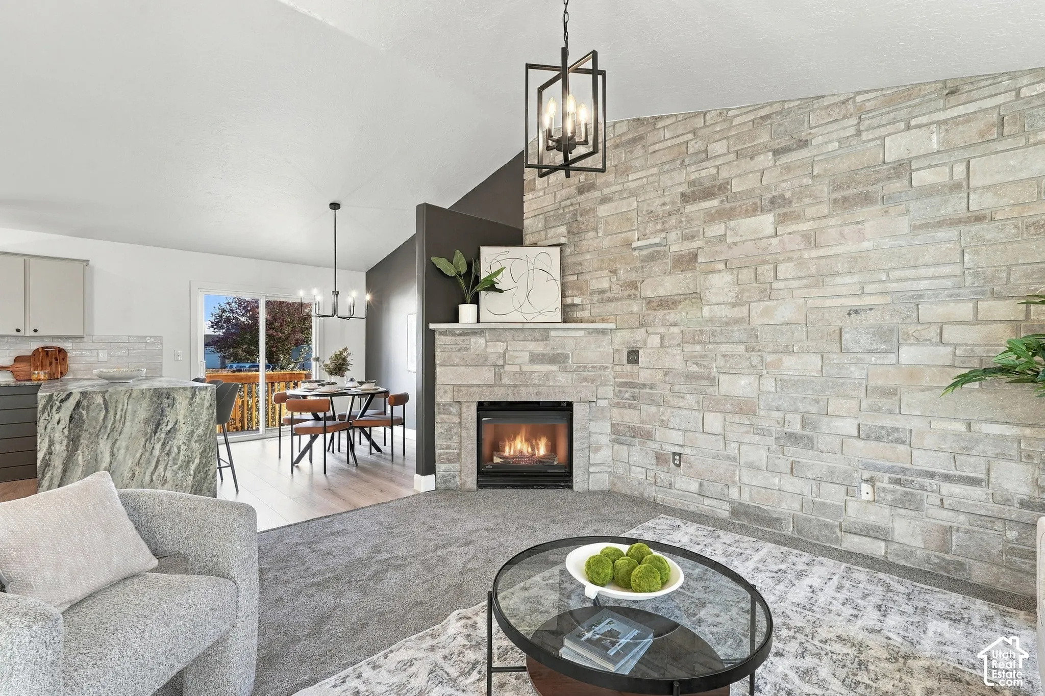 Full-height stone fireplace with a built-in firebox, vaulted ceilings, geometric iron chandelier, stone-surround kitchen island, and sliding glass doors
