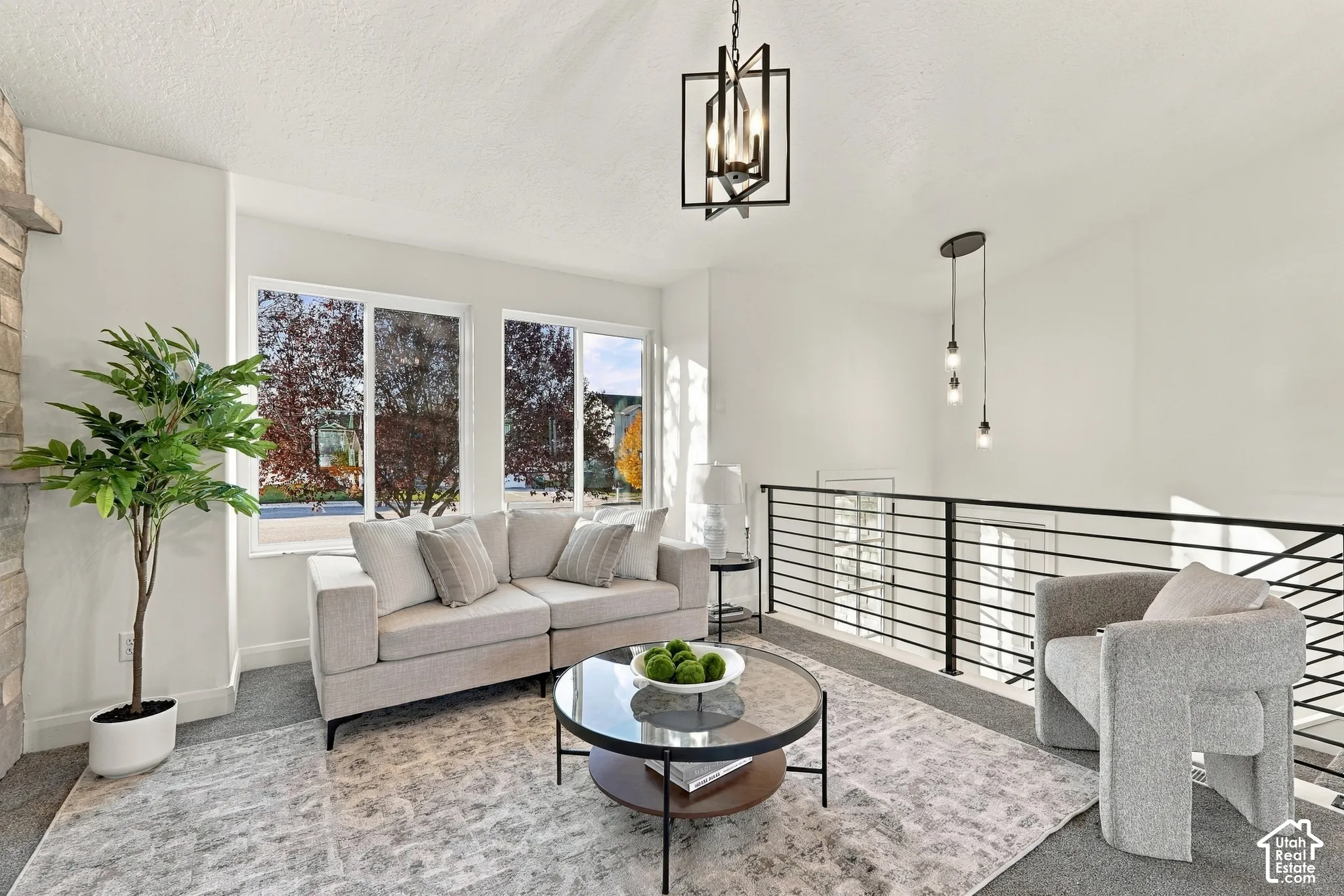 Living space featuring large windows, matte black metal horizontal railing, geometric pendant lighting, multi-bulb hanging fixture, and stacked stone masonry element