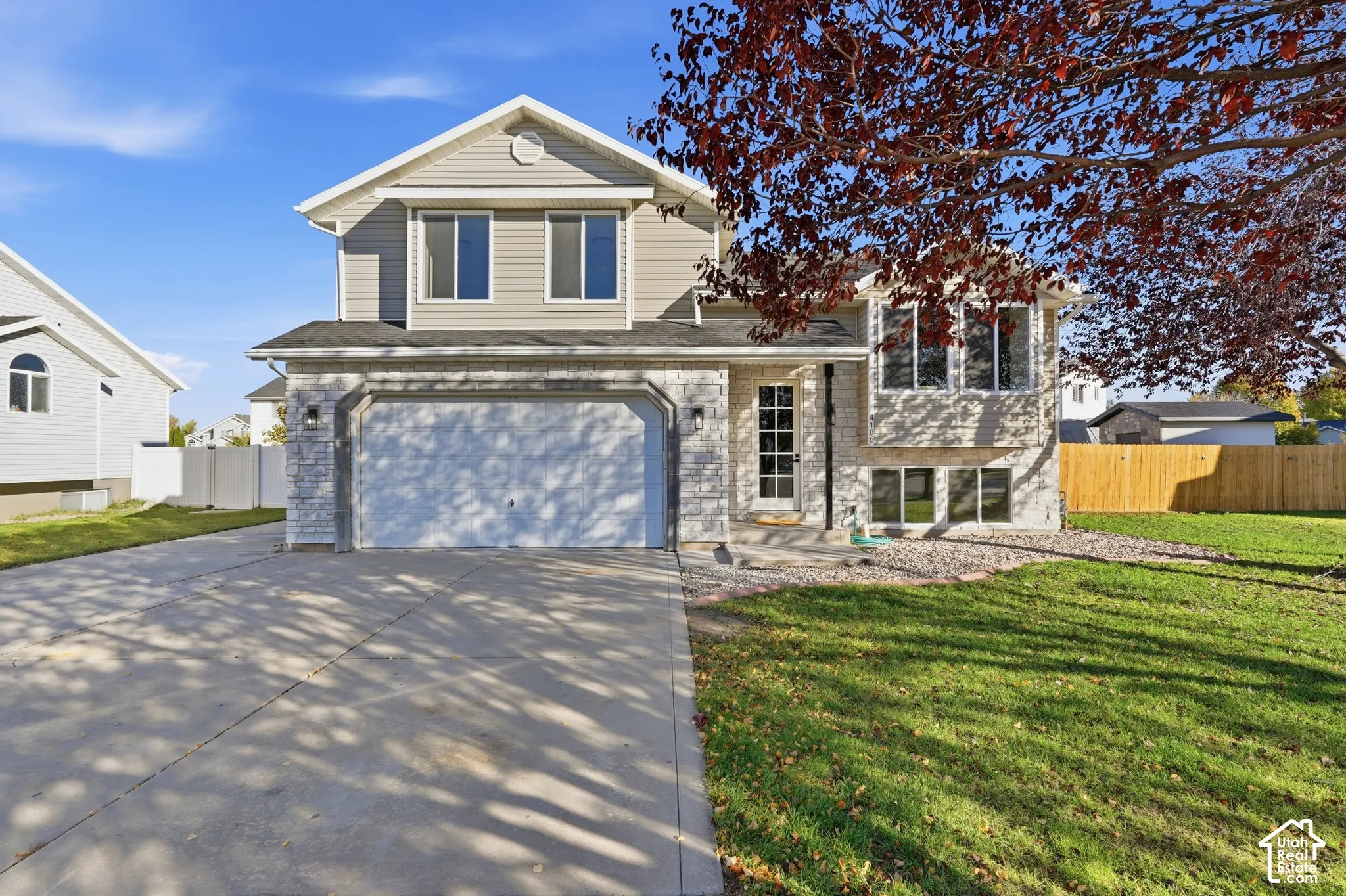 Two-story split-level exterior featuring a combination of horizontal siding and stone veneer, a concrete driveway, an attached two-car garage, and a multi-pane glass entry door
