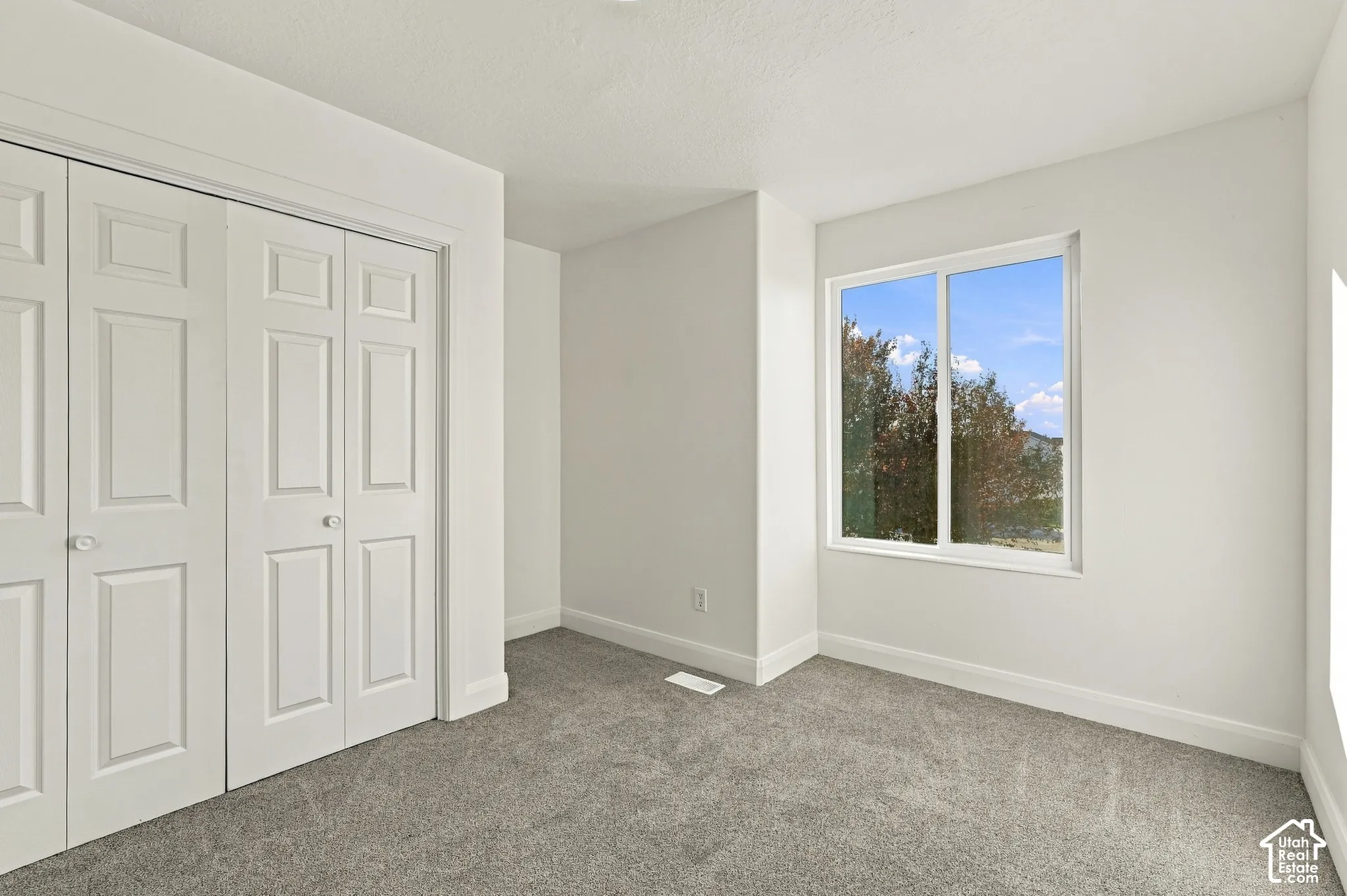 Neutral interior featuring wall-to-wall carpeting, white walls, dual bi-fold closet doors, and a sliding window