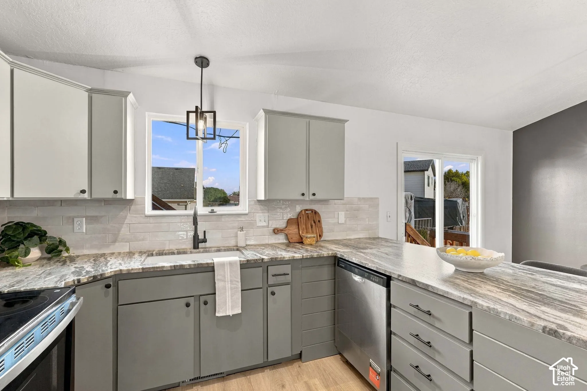 Kitchen featuring dual-tone cabinetry, stone-finish countertops, subway tile backsplash, stainless steel dishwasher, and matte black hardware