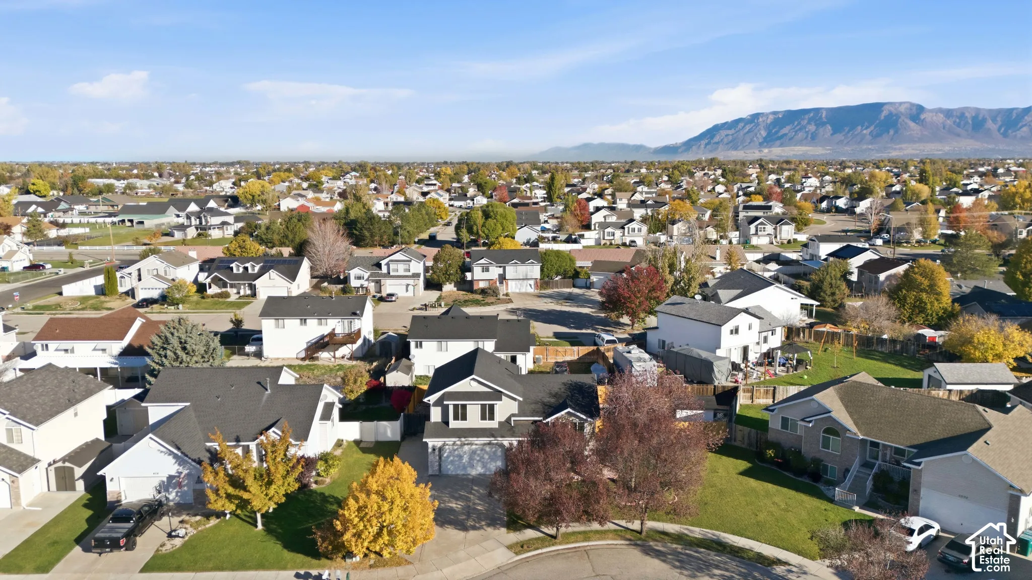 Aerial perspective featuring a multi-level suburban residence with an attached garage, asphalt roof, and mountainous backdrop
