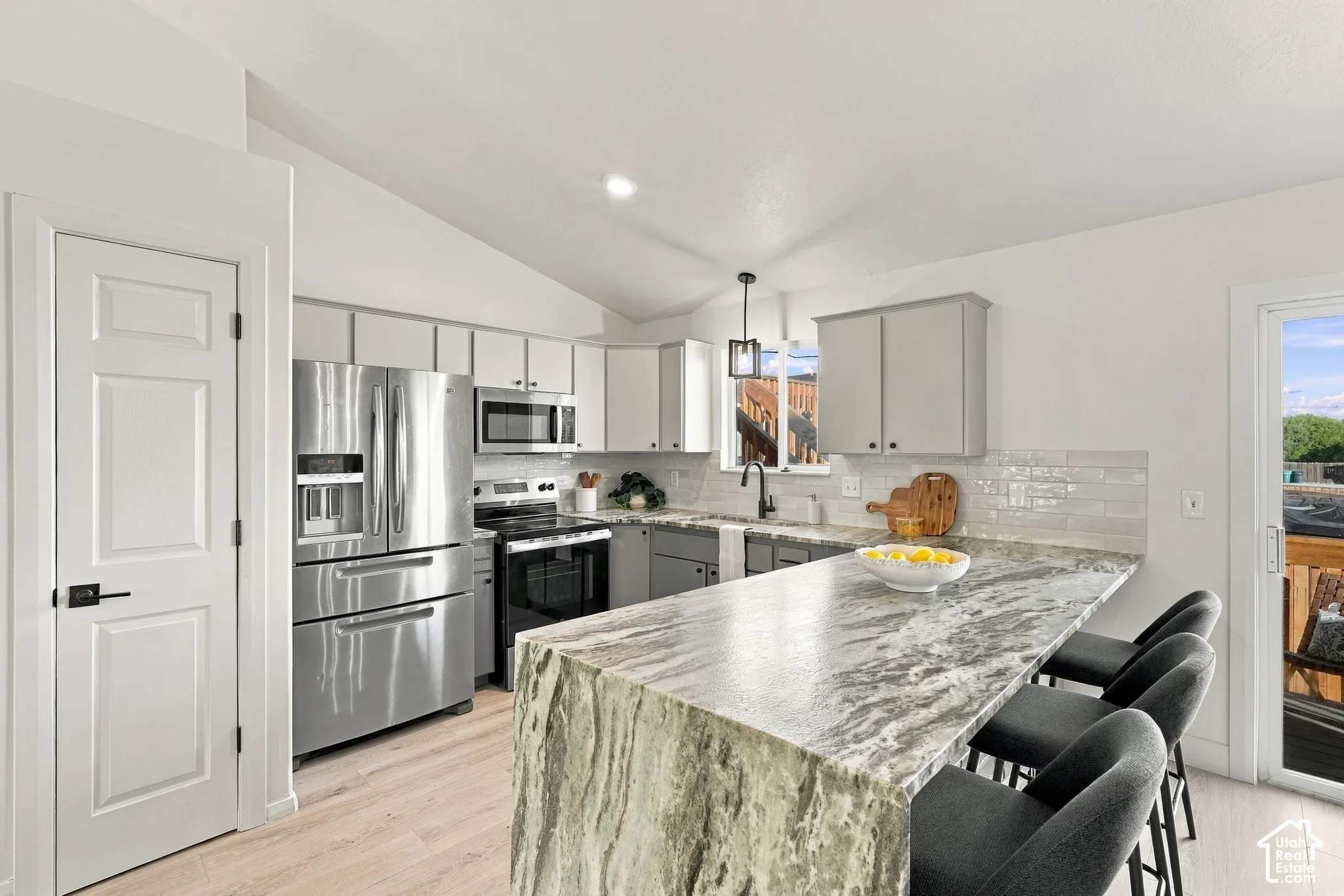 Kitchen featuring a stone-topped island, light wood-finish flooring, two-tone cabinetry, stainless steel appliances, and a glass-paneled exterior door