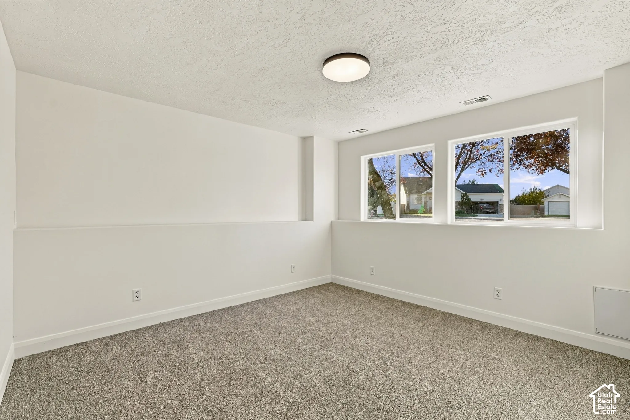 Neutral interior space featuring crisp white walls, neutral-toned wall-to-wall carpeting, dual sliding windows, and a flush-mount ceiling light