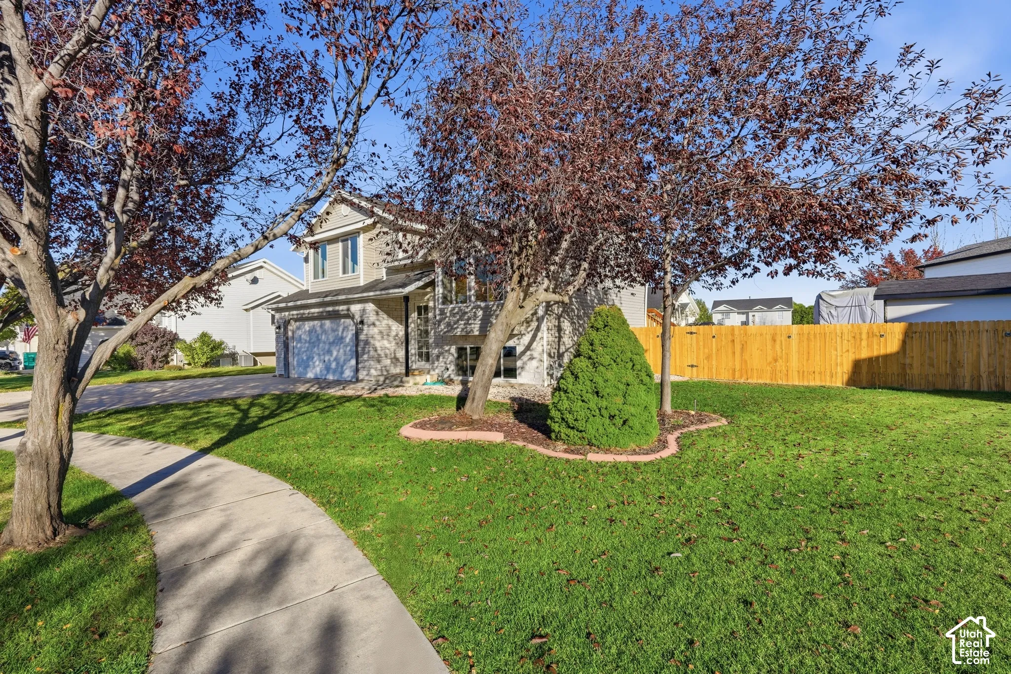 Two-story residence featuring a partial stone facade, attached two-car garage, manicured lawn, established landscaping, and wooden privacy fencing