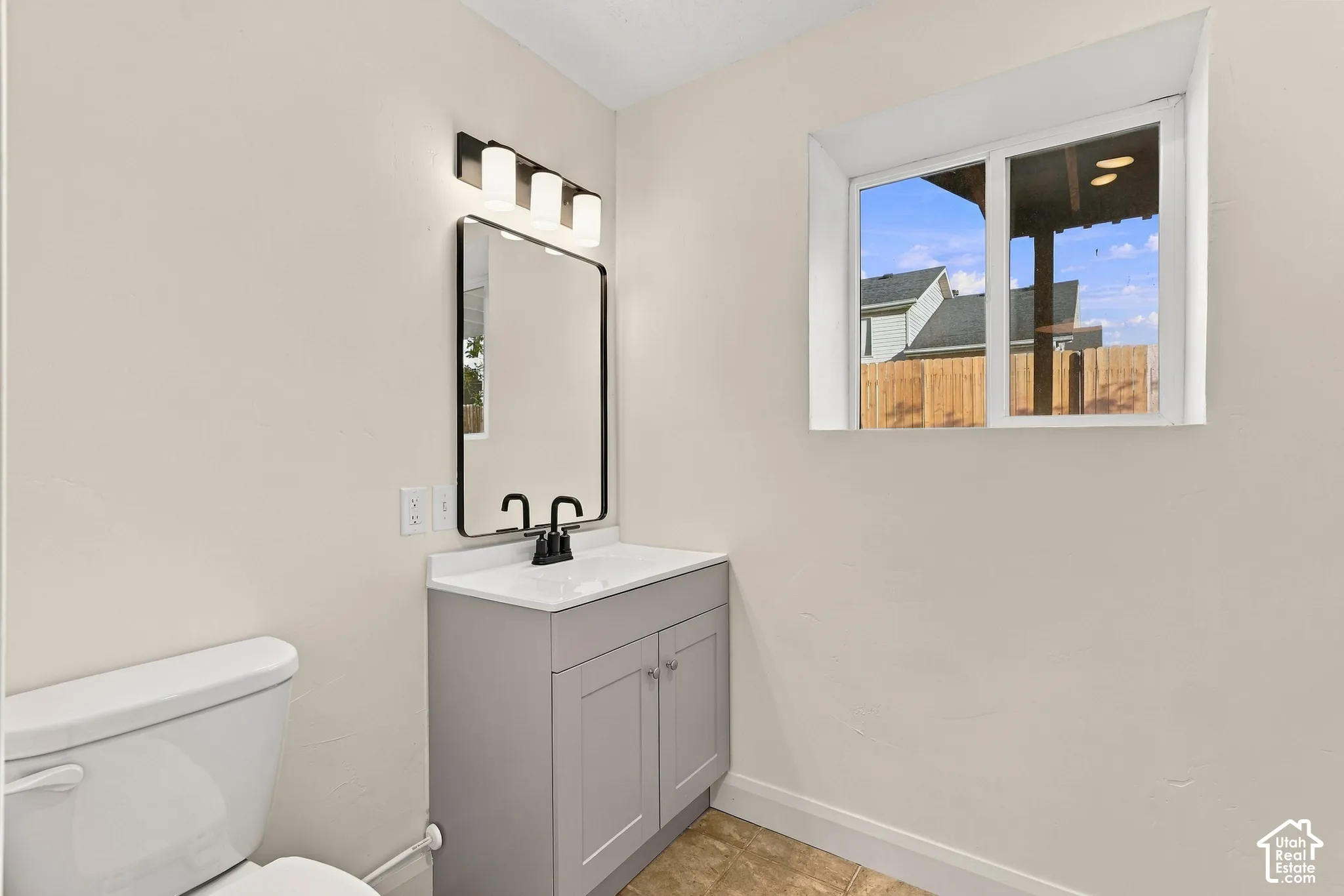 Bathroom featuring a gray vanity cabinet, white countertop with an integrated basin, matte black faucet and mirror frame, three-light vanity fixture, and window