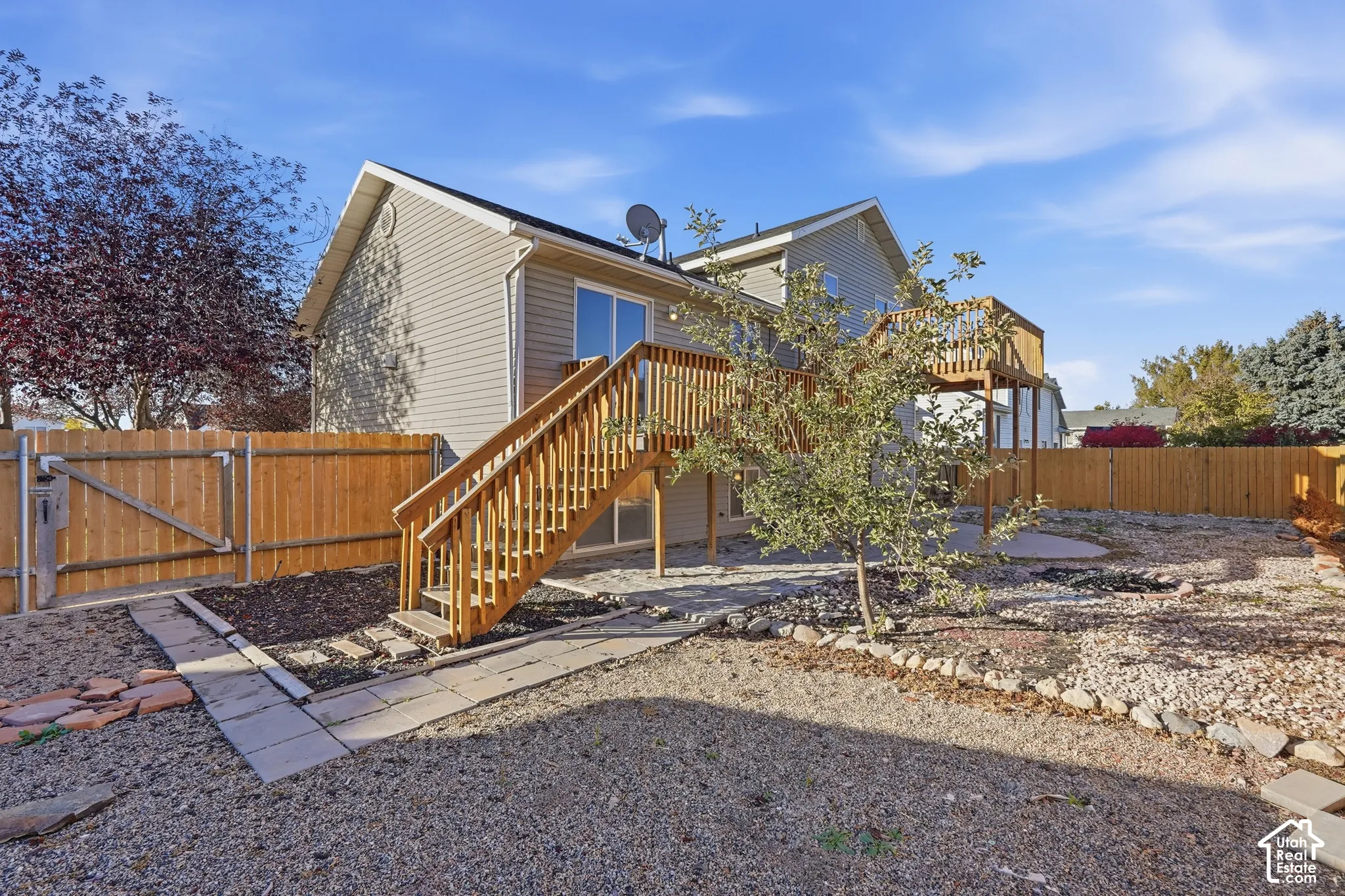 Exterior siding with a wood-framed elevated deck, staircase, concrete patio, and fenced backyard with stone landscaping