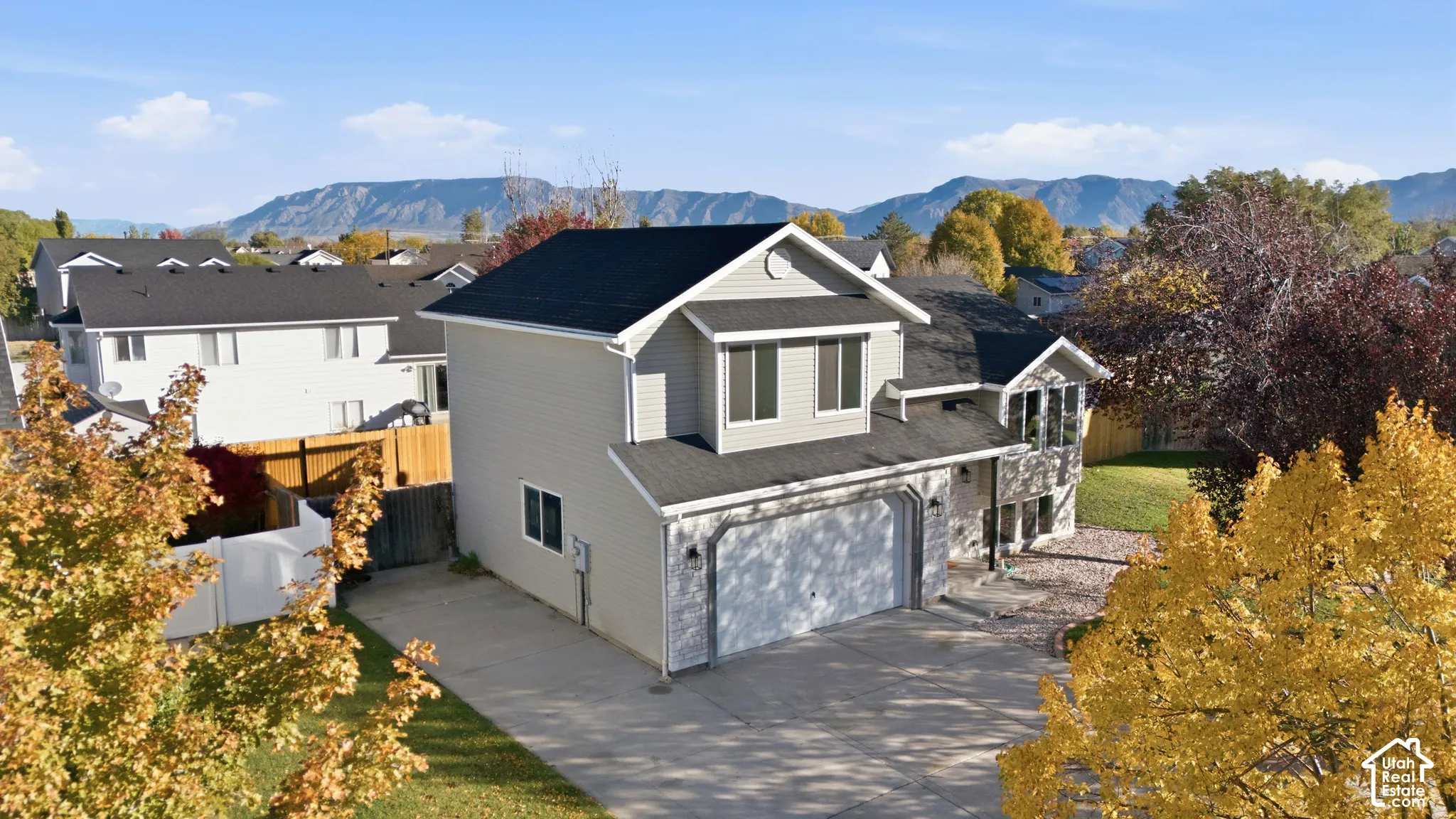 Two-story residence featuring light-toned horizontal siding, a multi-gabled roofline, an attached two-car garage, and a concrete driveway, set against a backdrop of distant mountains