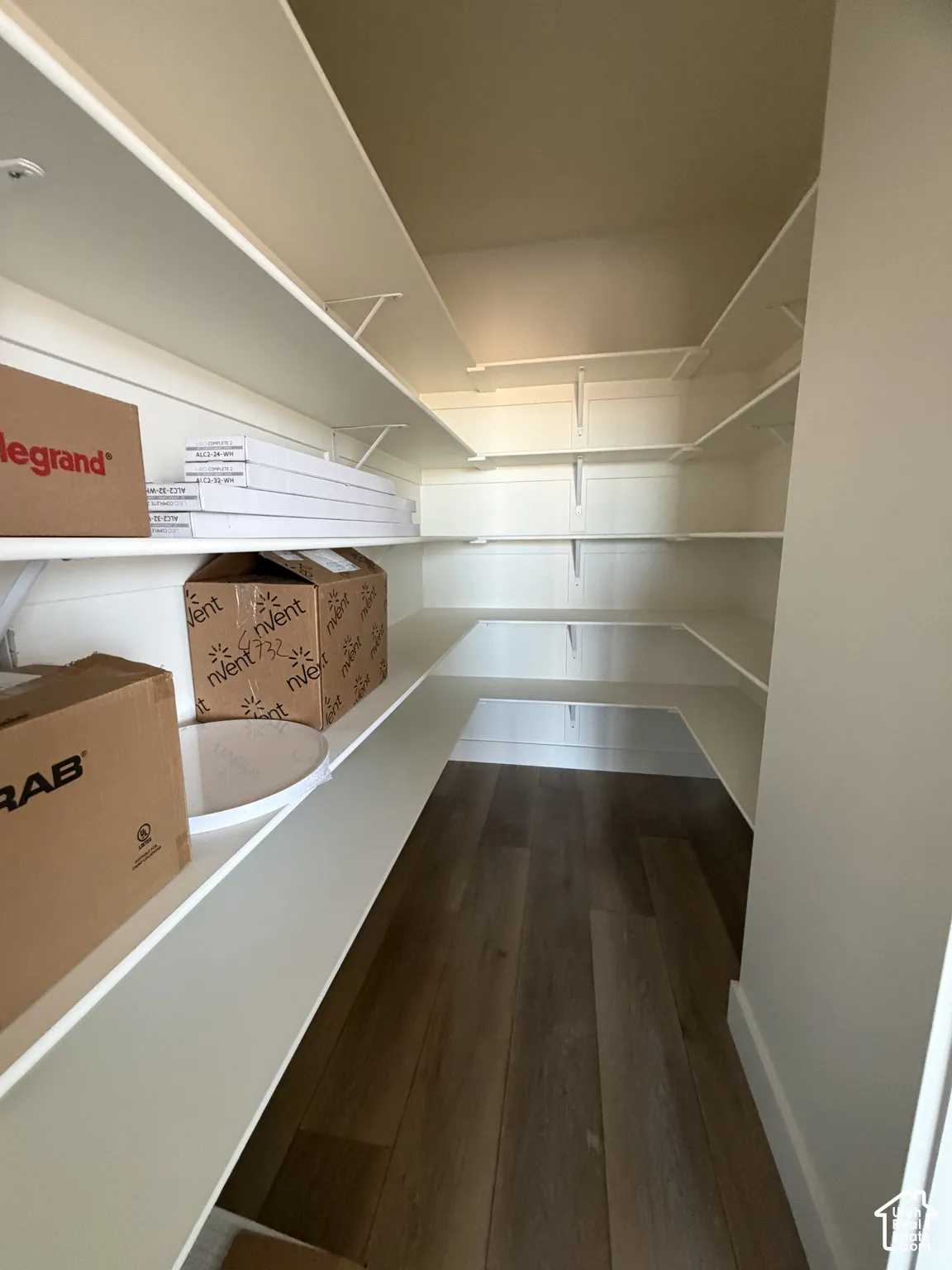 Walk-in storage space featuring multi-level white shelving and wood-finish flooring