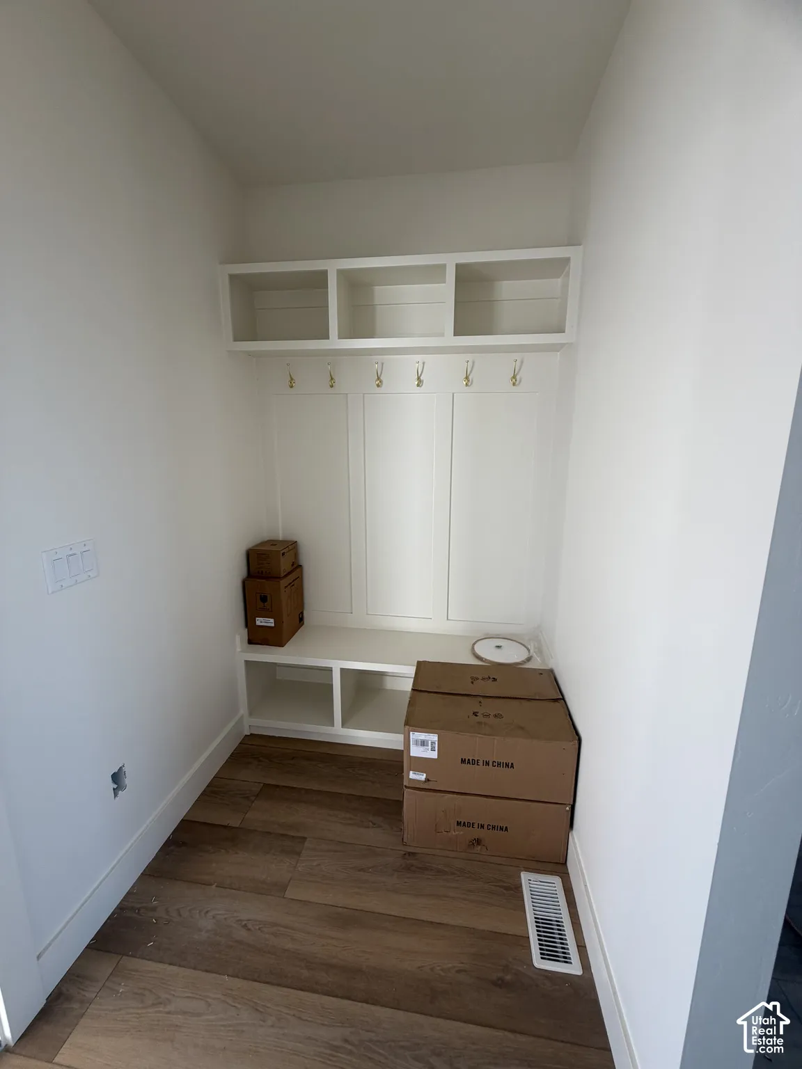 Built-in mudroom bench with paneled backing, integrated overhead storage cubbies, and brass-finish wall hooks, complemented by wood-finish flooring