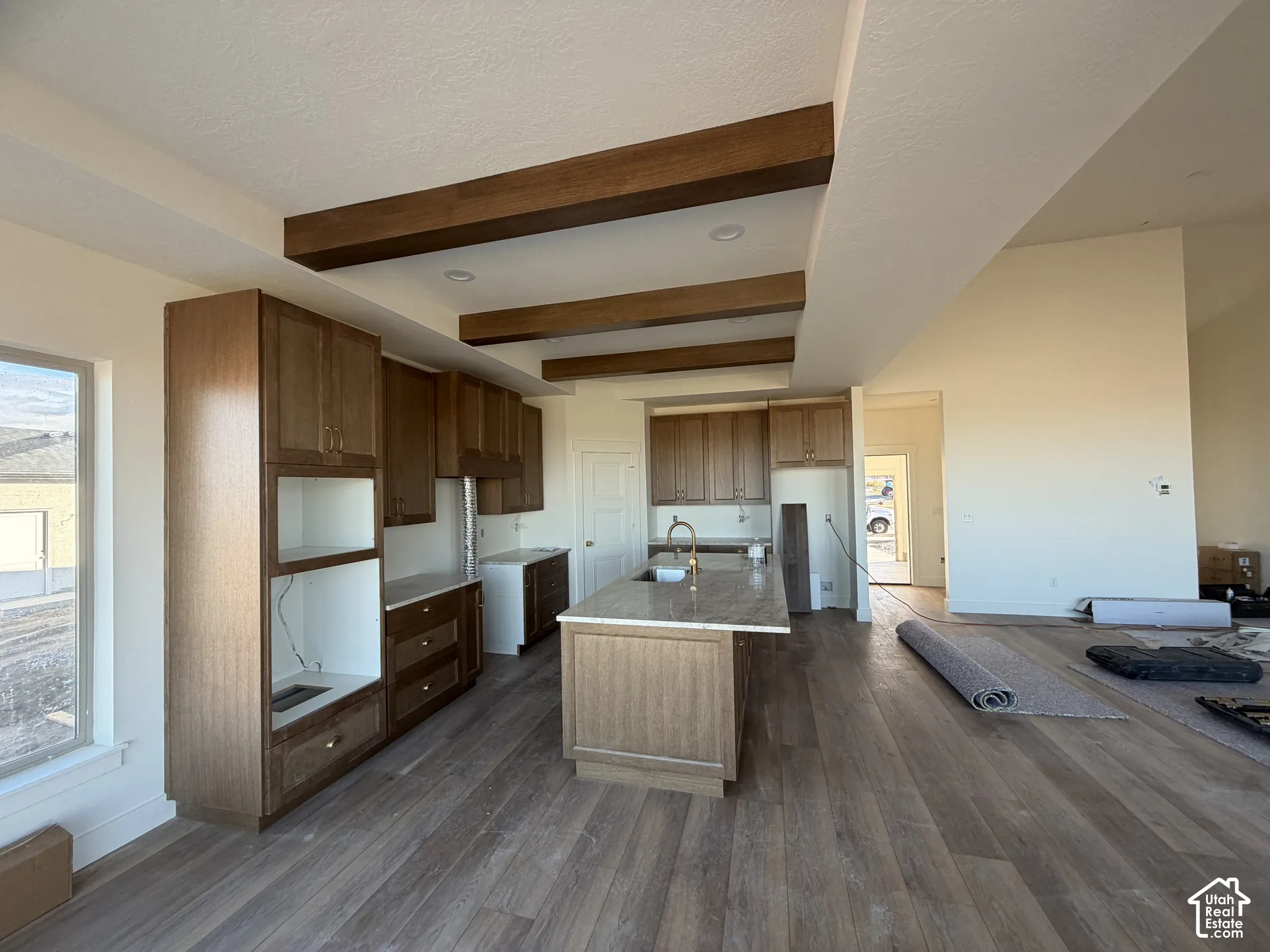 Kitchen featuring wood-finish cabinetry, central island with stone-surface countertop, recessed ceiling lighting, decorative wood-finish ceiling beams, and wood-finish flooring