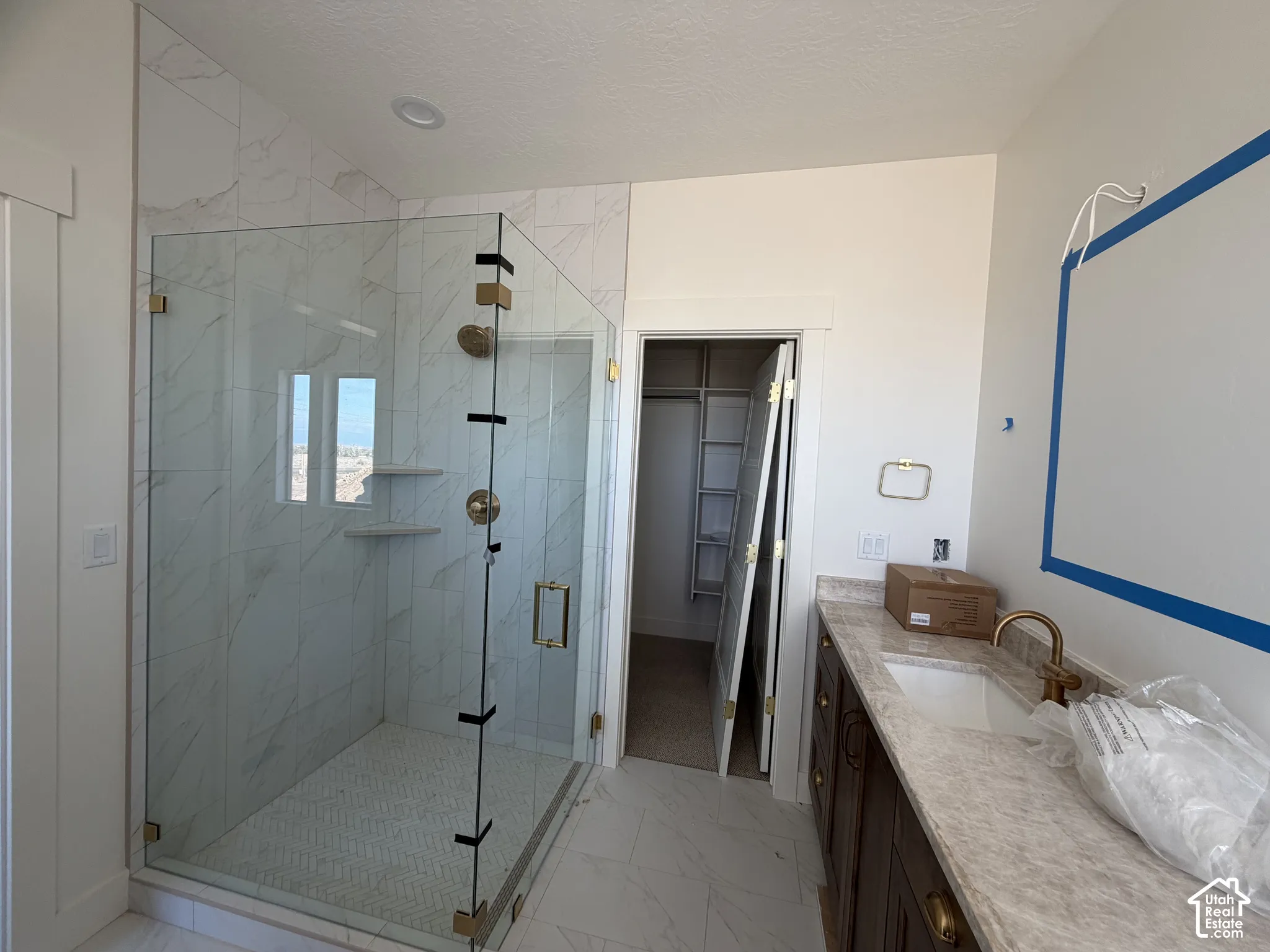 Walk-in shower with floor-to-ceiling tile surround and integrated shelving, stone-finish vanity countertop with undermount sink, brass-tone hardware, and custom walk-in closet with built-in shelving