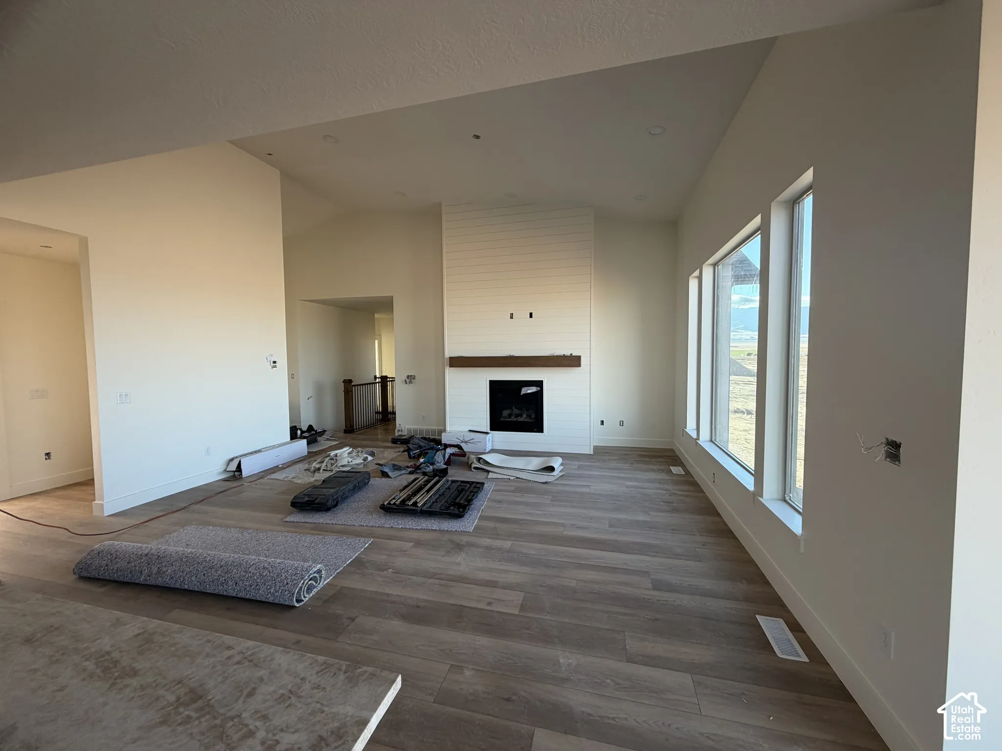 Vaulted ceilings, wood-finish flooring, shiplap fireplace surround with wood mantel, and large picture windows
