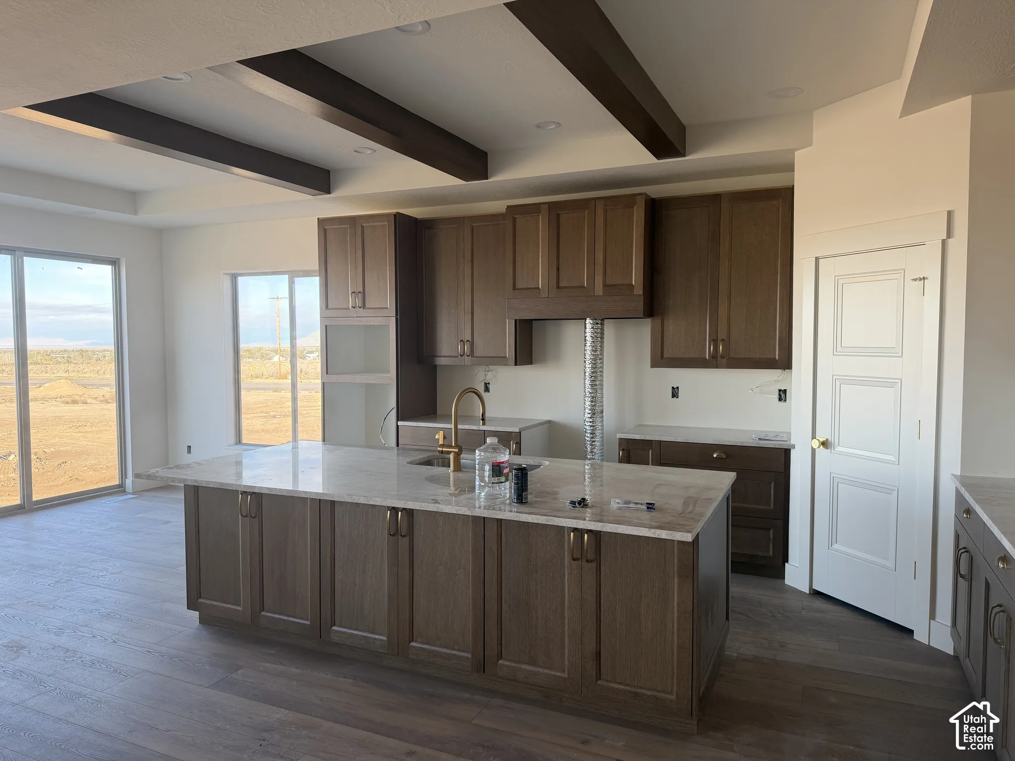 Kitchen featuring stained wood cabinetry, stone-surface island, wood-finish flooring, and recessed ceiling beams