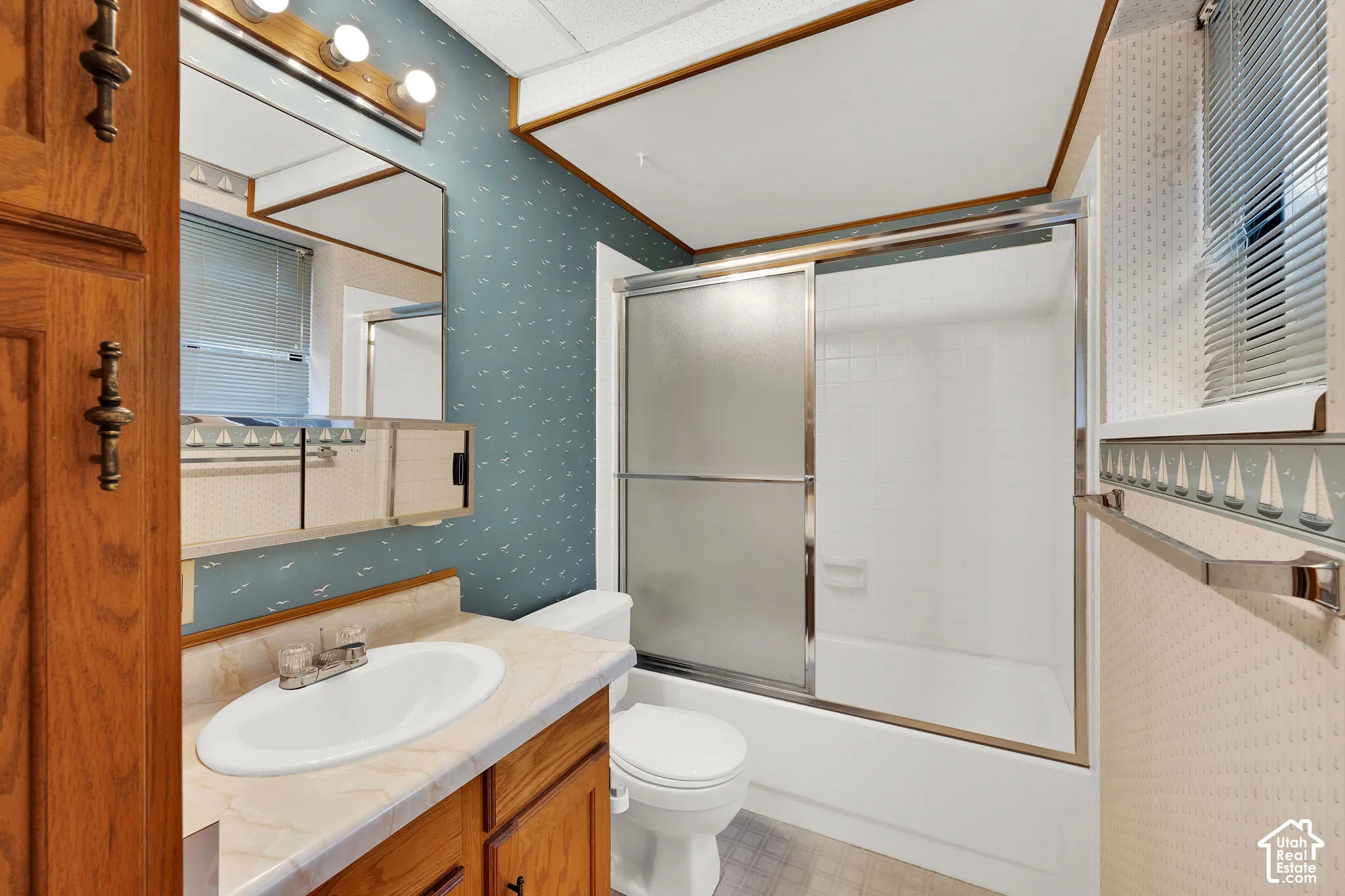 Bathroom featuring a wood-finish vanity with a light-toned countertop, integrated basin, a wall-mounted mirror with integrated lighting, and a bathtub with sliding glass doors
