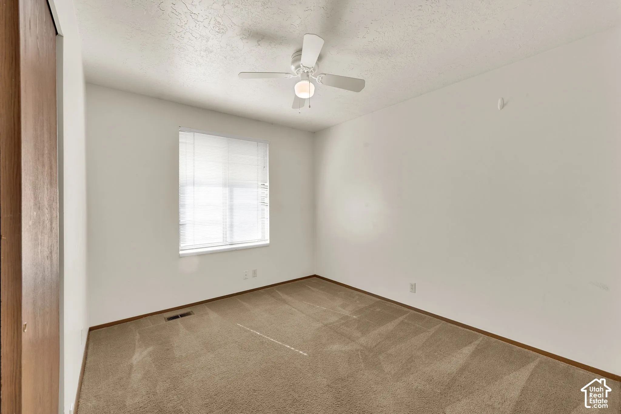 Neutral-toned wall-to-wall carpeting, white walls, ceiling fan with integrated lighting, and horizontal window blinds