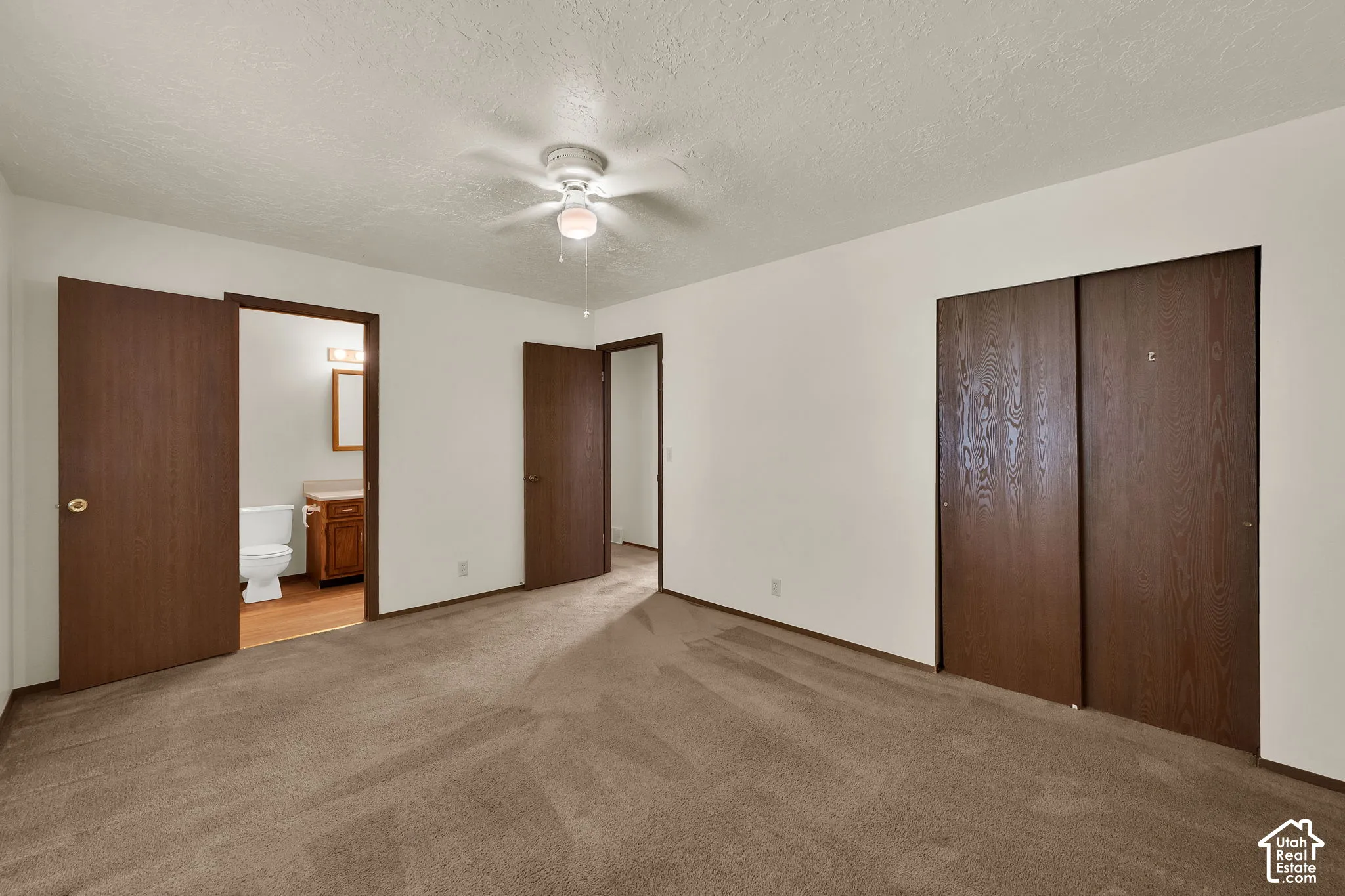 Carpeted room featuring a ceiling fan with integrated lighting, wood-finish sliding closet doors, and wood-finish interior doors