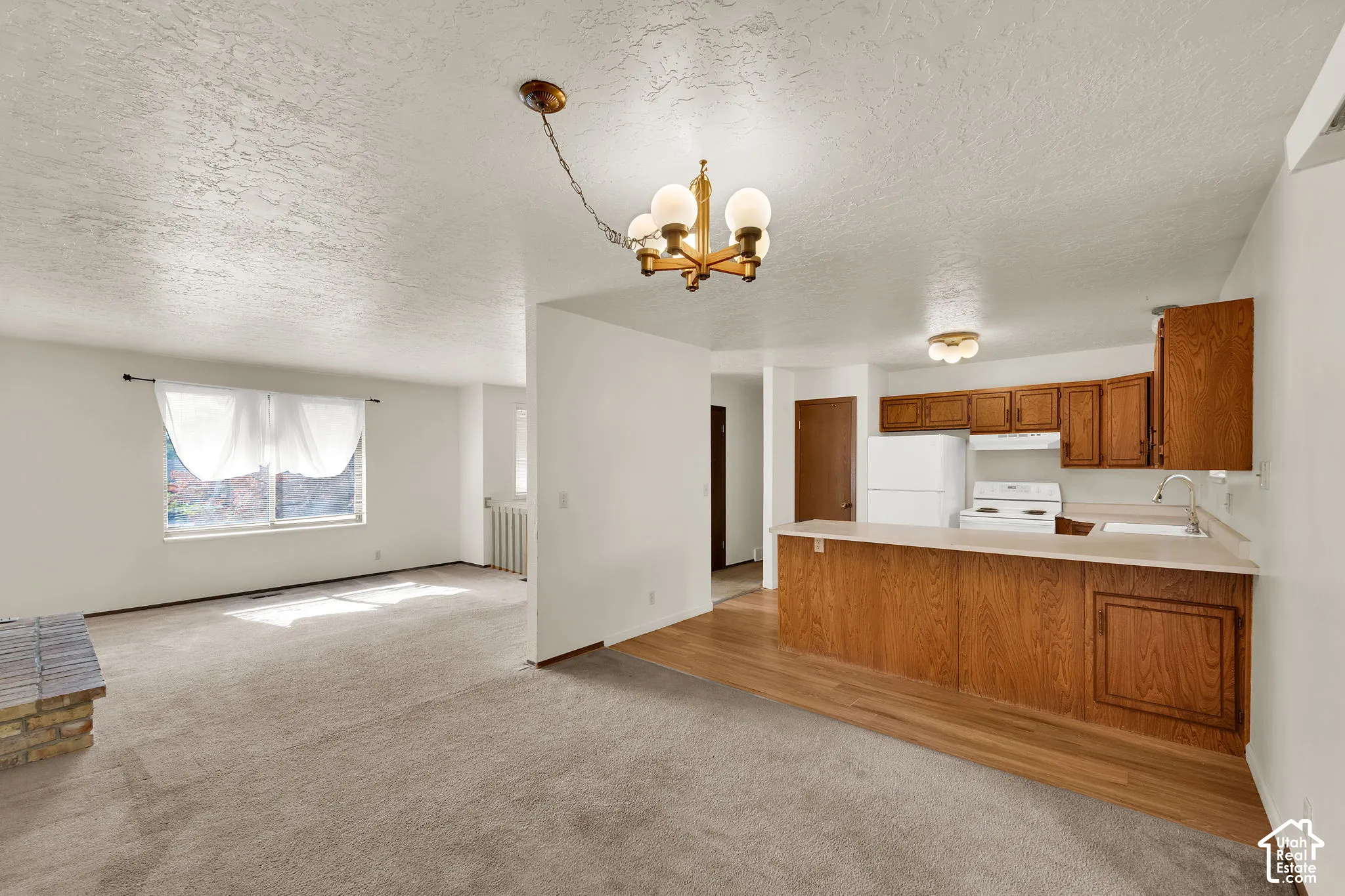 Kitchen featuring a peninsula counter, wood-finish cabinetry, and built-in appliances, paired with a living area including a brick-surround fireplace and multi-arm lighting fixtures