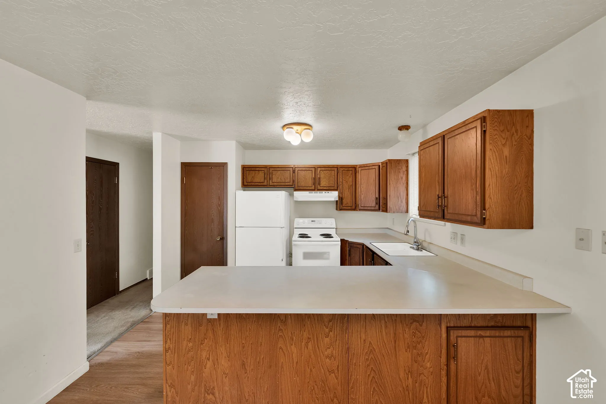 Kitchen featuring wood cabinetry, a peninsula countertop, white appliances, and a dual-handle faucet