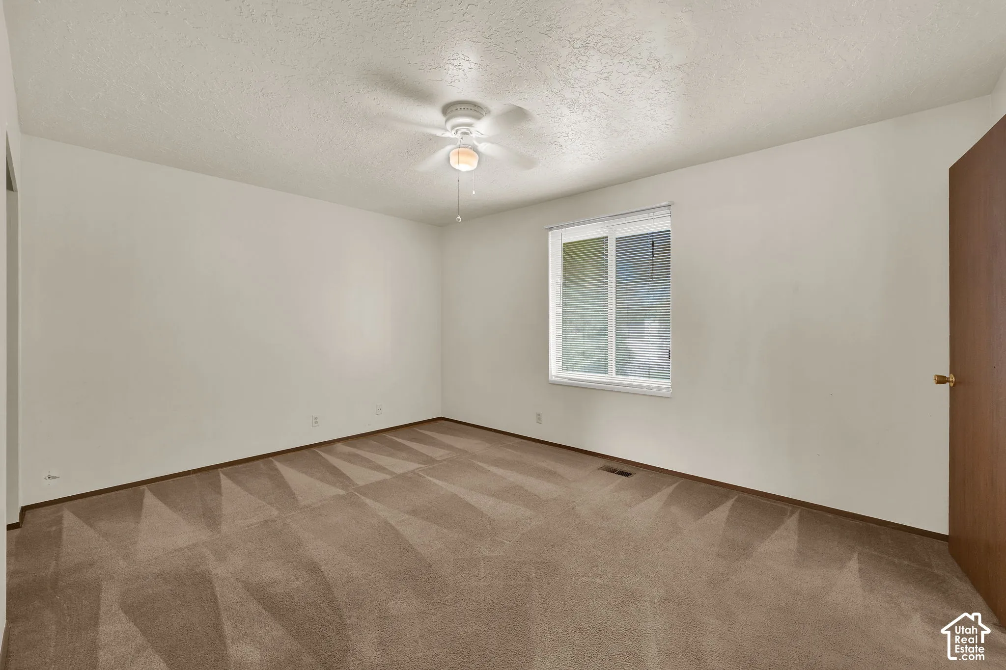 Neutral wall finishes, textured carpeted flooring, a single-pane sliding window, and a ceiling-mounted light fixture with a fan