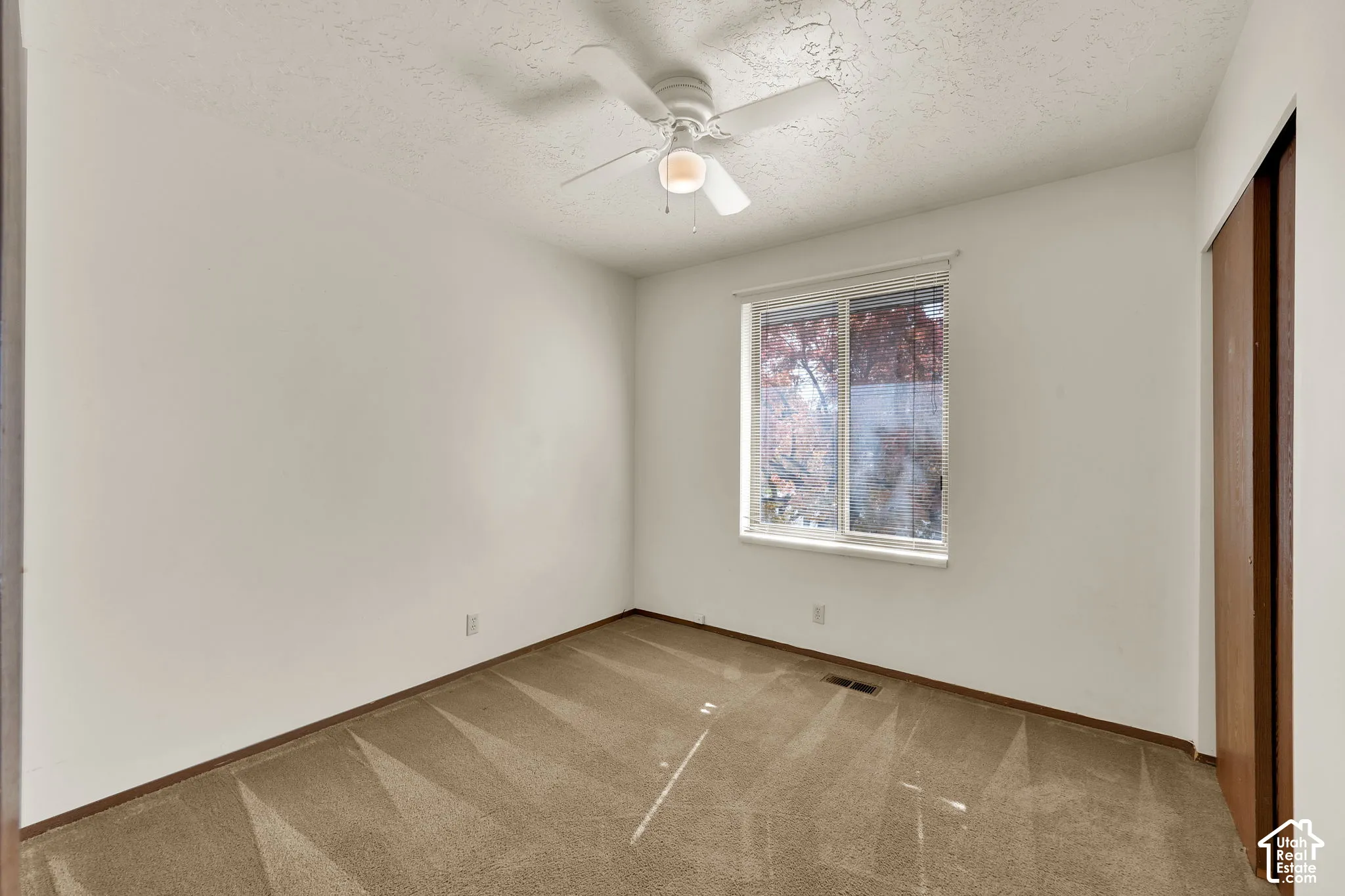 Neutral-toned carpeted flooring, sliding wood-finish closet doors, ceiling fan with integrated lighting, and a single-pane window