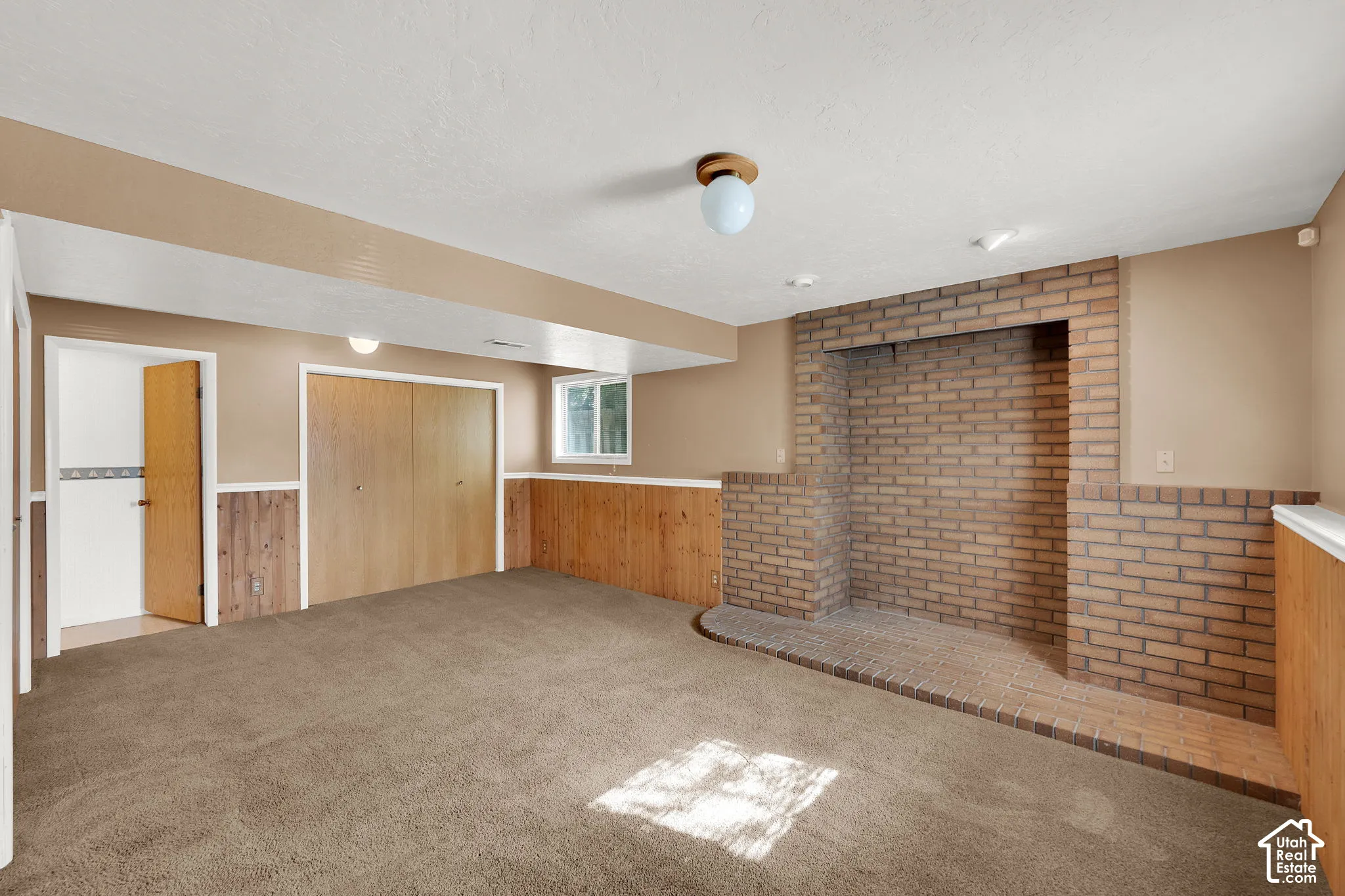 Interior room featuring brick masonry fireplace surround, wood-panel wall treatments, wall-to-wall carpeting, and dual-door built-in storage
