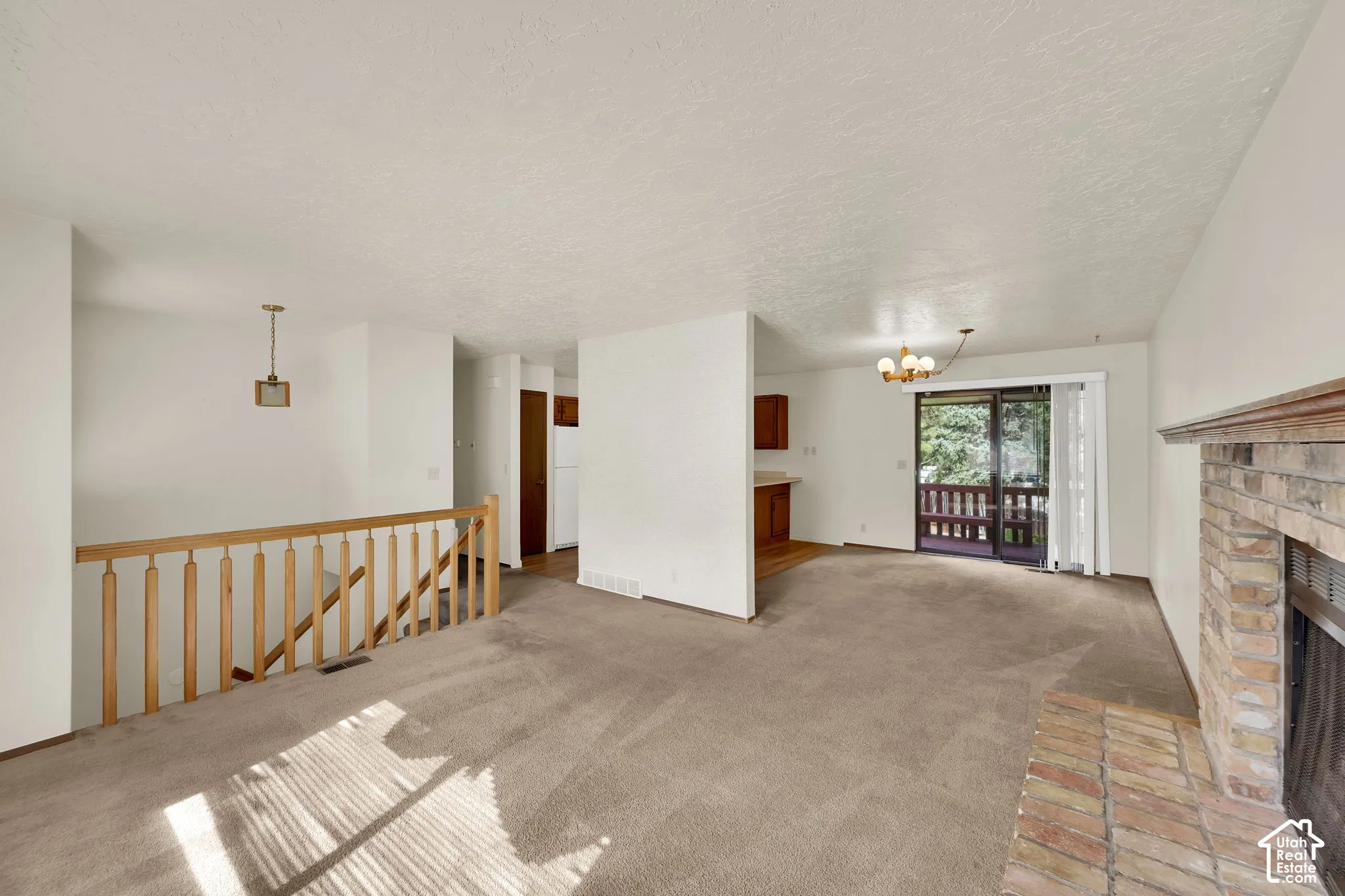 Brick fireplace with a wooden mantel, sliding glass doors, wooden staircase railing, and built-in kitchen cabinetry