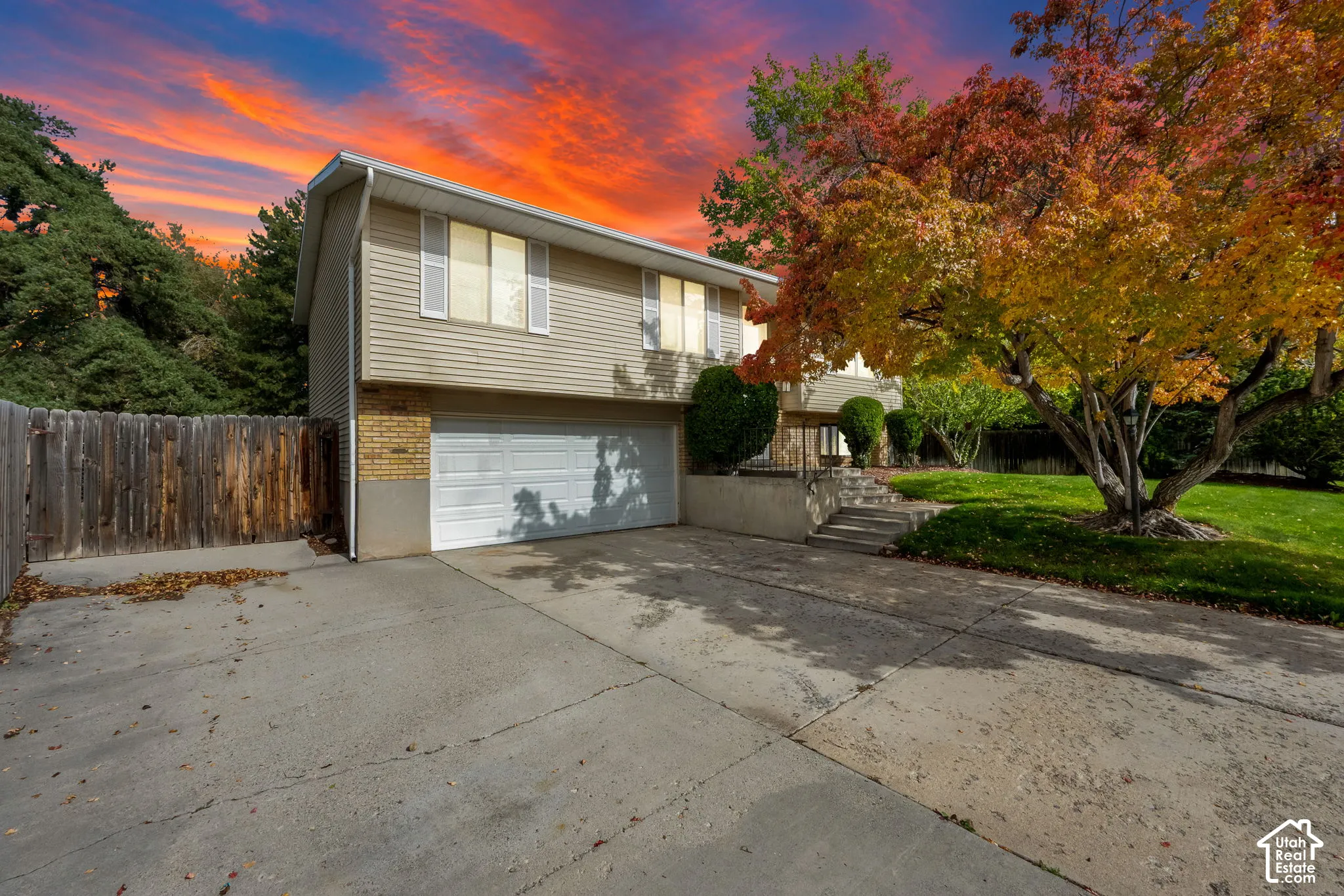Split-level exterior featuring horizontal siding, a brick lower facade, an attached two-car garage, concrete driveway, and wood-fence enclosure