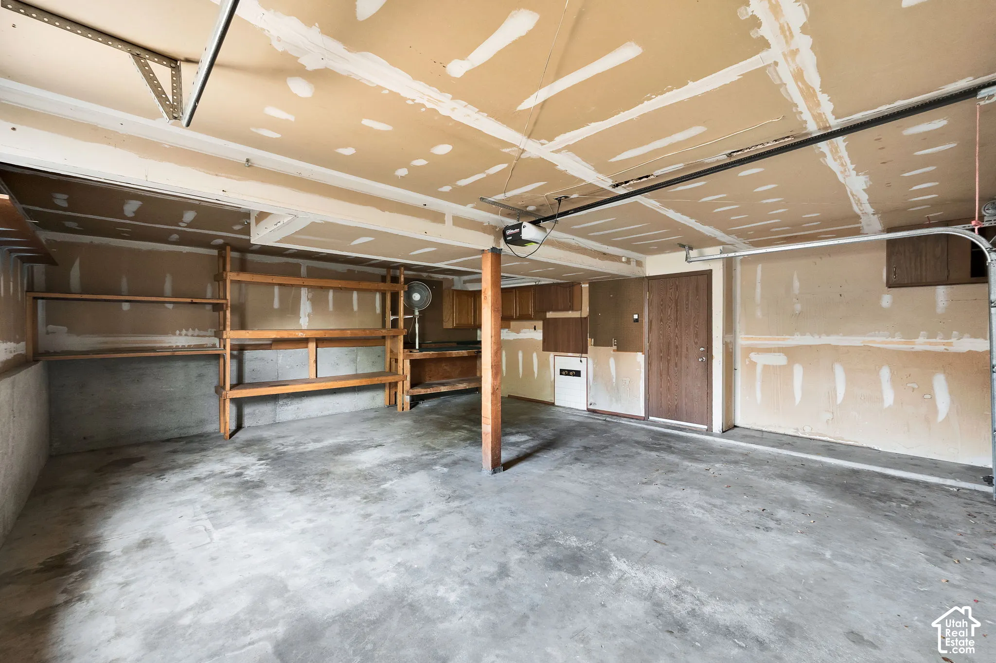 Multi-car garage featuring a concrete floor, built-in wooden shelving units, an automatic garage door opener, and a dedicated entry door