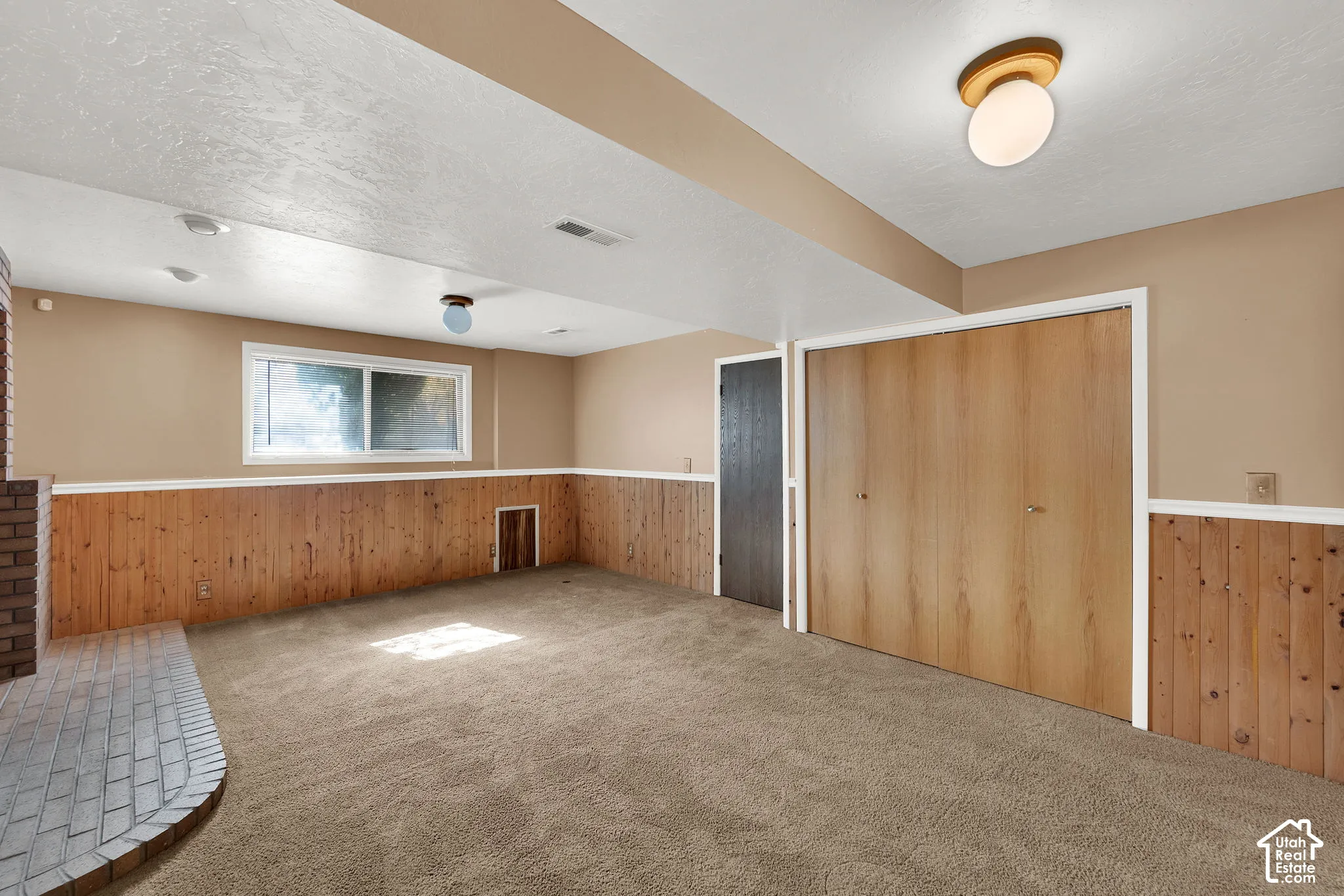 Interior space featuring wood-panel wainscoting, floor-to-ceiling brick hearth, sliding closet doors, wall-to-wall carpeting, and flush-mount lighting fixtures