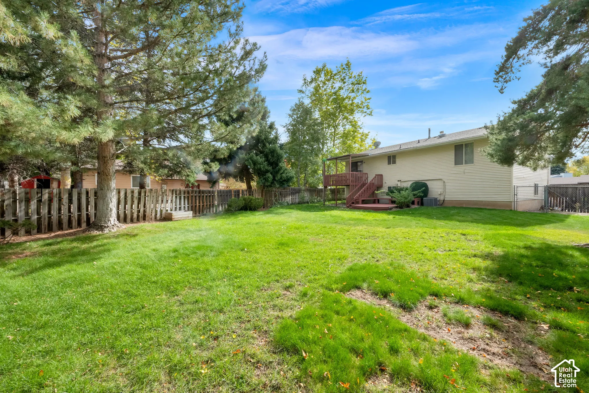 Backyard featuring a manicured lawn, mature trees, wood-slat perimeter fencing, and an elevated wooden deck