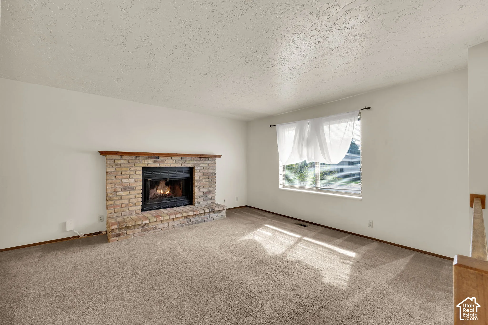 Living area featuring neutral carpeting, a masonry fireplace with a wood mantel, and a large window