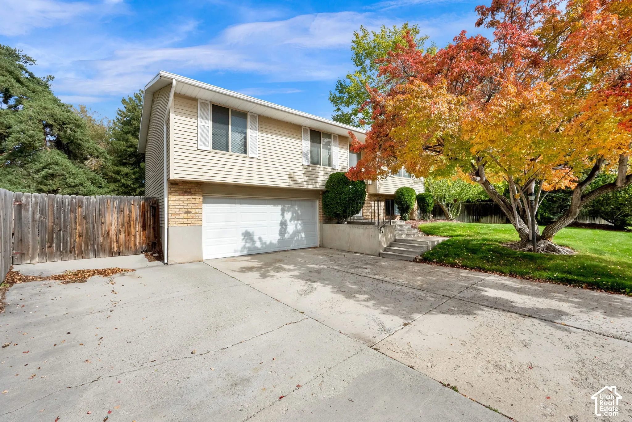 Split-level exterior featuring light-toned horizontal siding, a multi-car garage, concrete driveway, and wood-panel fencing