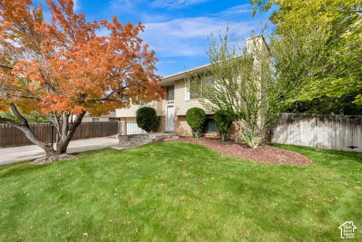 Split-level exterior featuring light-toned horizontal siding, a stone facade accent, concrete stairs with iron handrails, a paved driveway, and mature landscaping