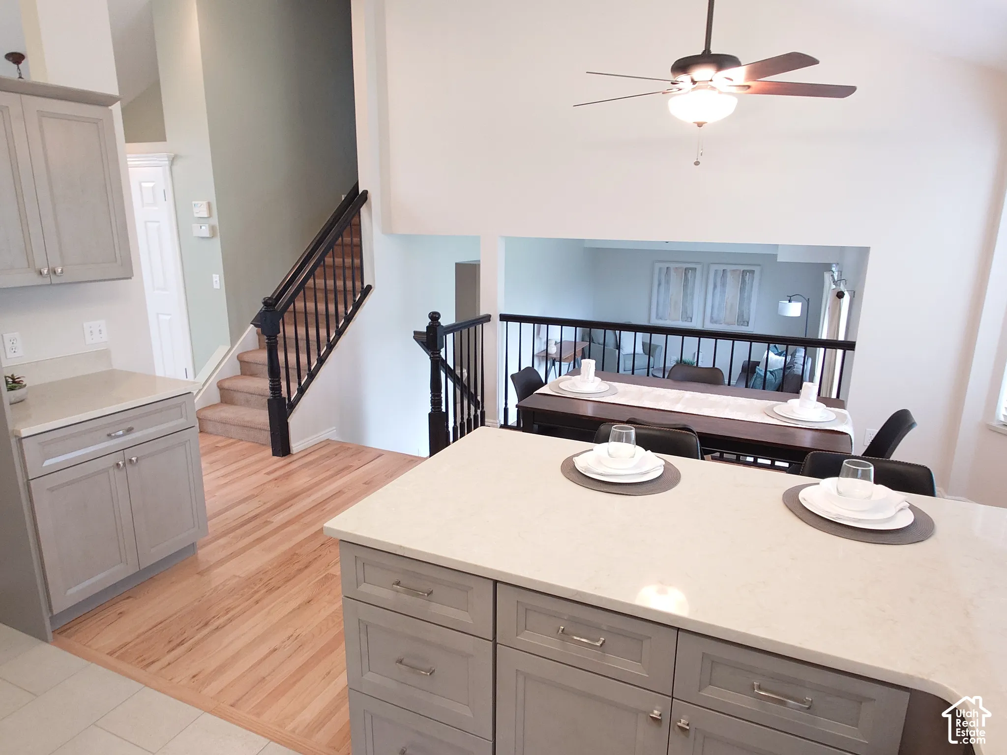 Kitchen island with stone-finish countertop and shaker-style cabinetry, high vaulted ceilings, wood-finish flooring, and a staircase with dark-finished railings