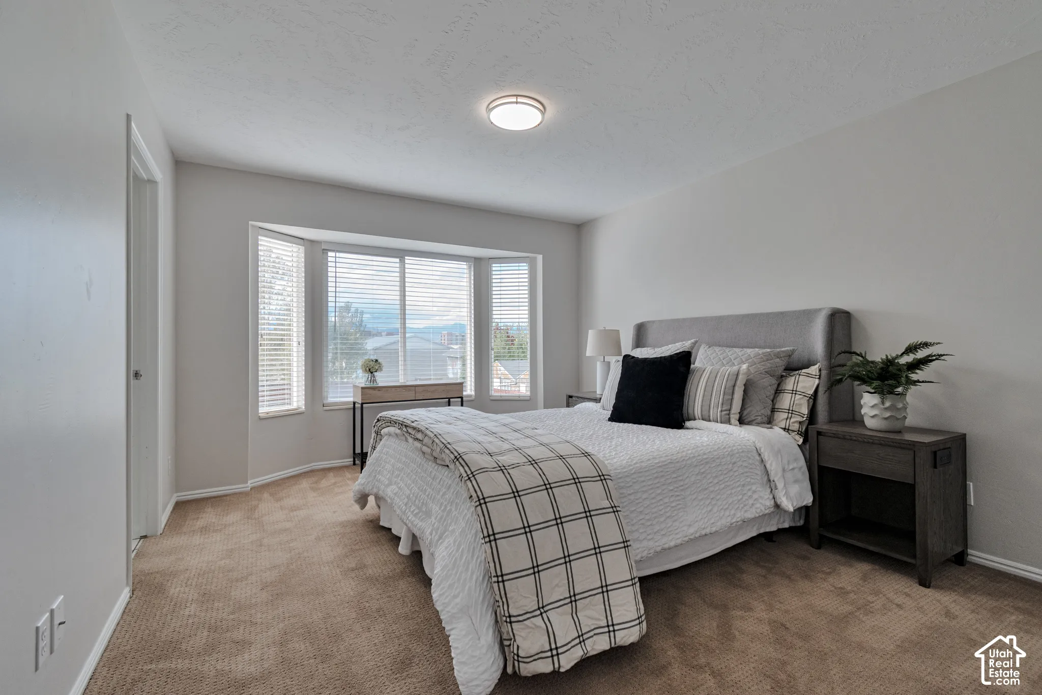 Neutral interior featuring neutral wall paint, wall-to-wall carpeting, a three-panel bay window, and a flush-mount overhead light fixture