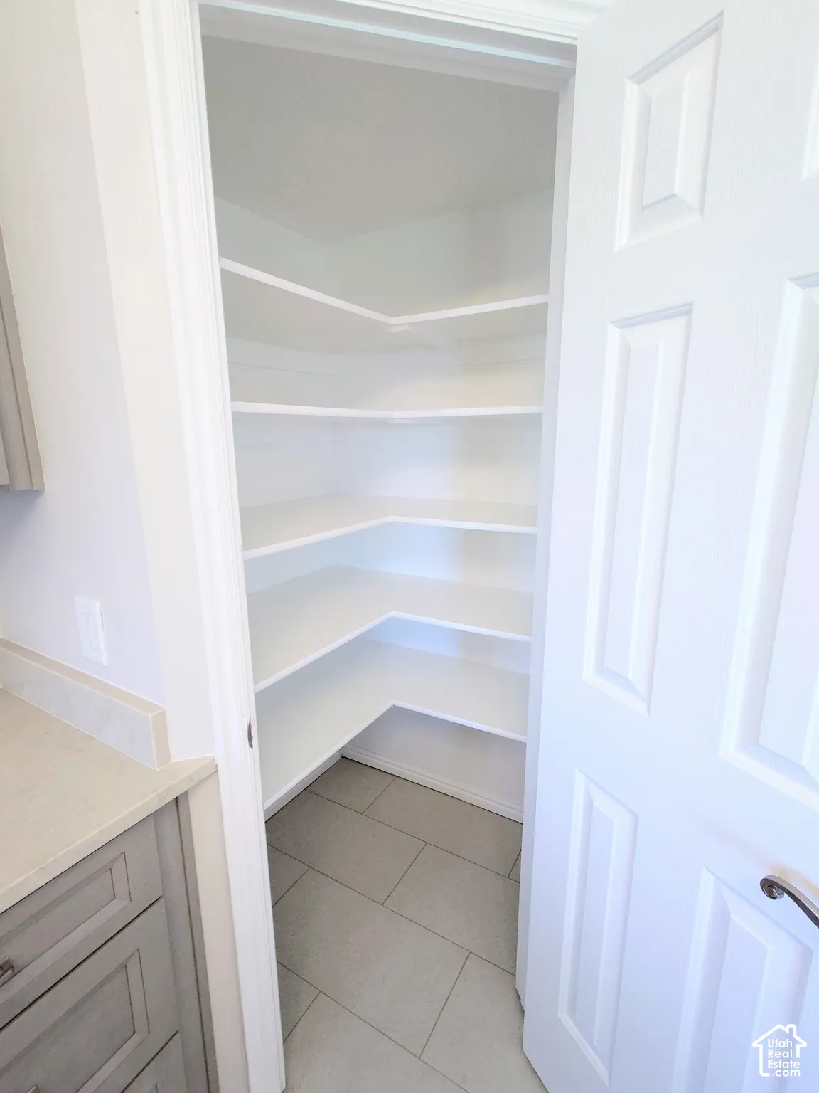 Walk-in pantry featuring white wrap-around shelving and neutral tile flooring, accessed by a paneled door