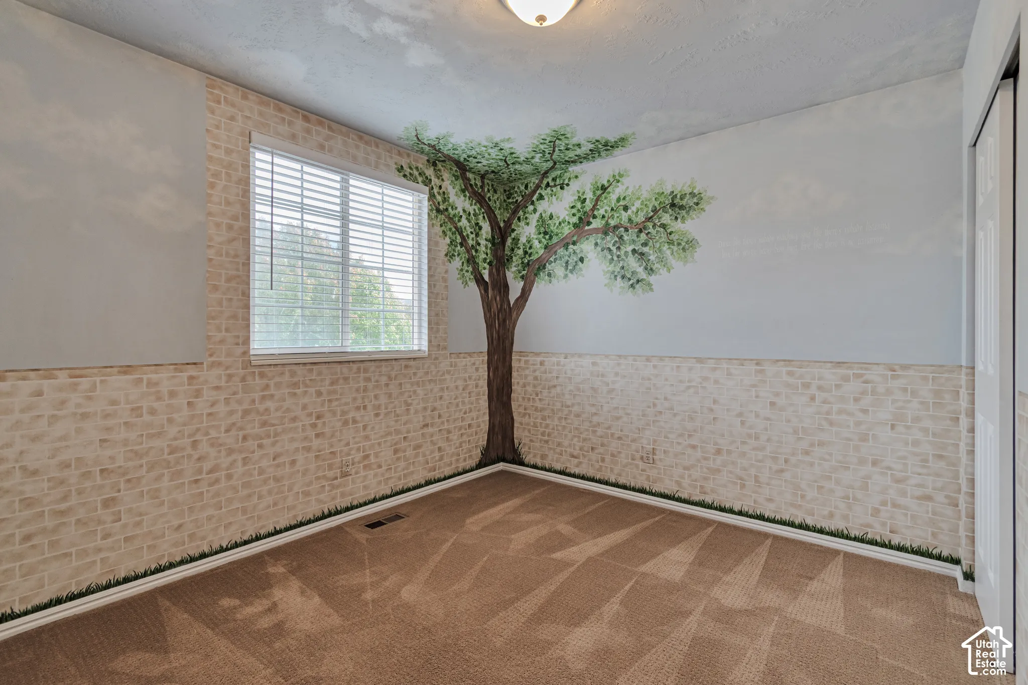 Textured wall detailing featuring faux-brick wainscoting, neutral carpeting, horizontal blind window treatment, and a painted wall mural