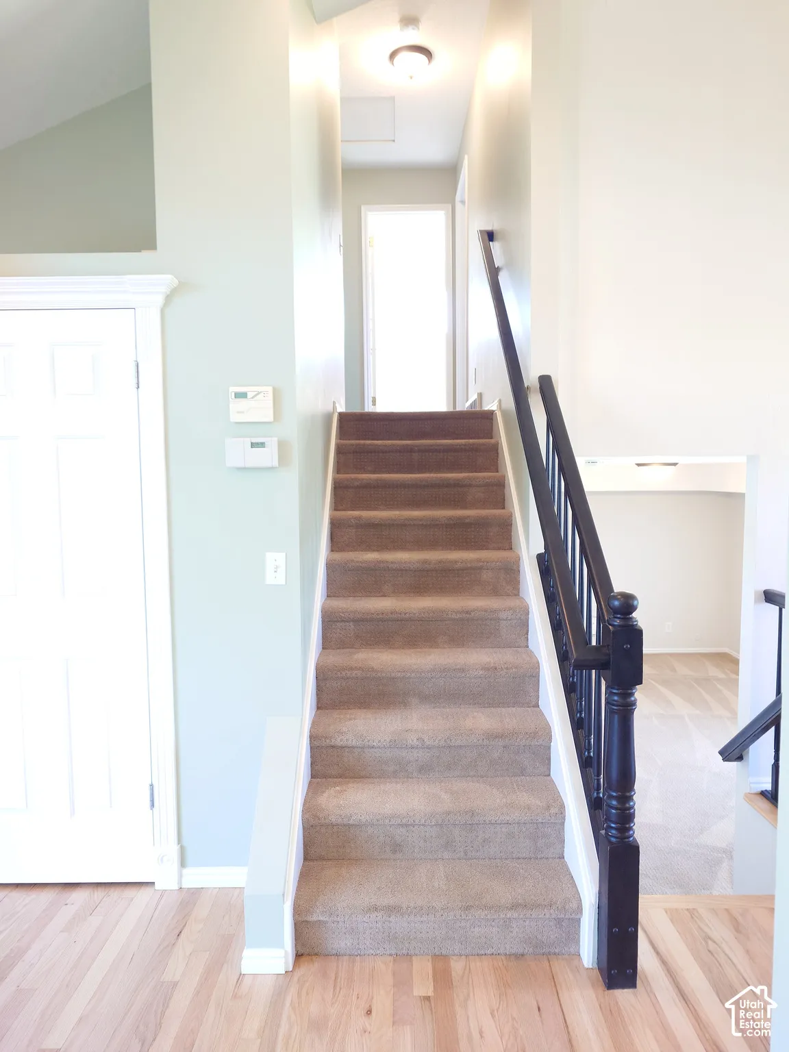 Staircase with carpeted steps, dark-finished wood handrail, decorative balusters, light-colored walls, and wood-finish flooring