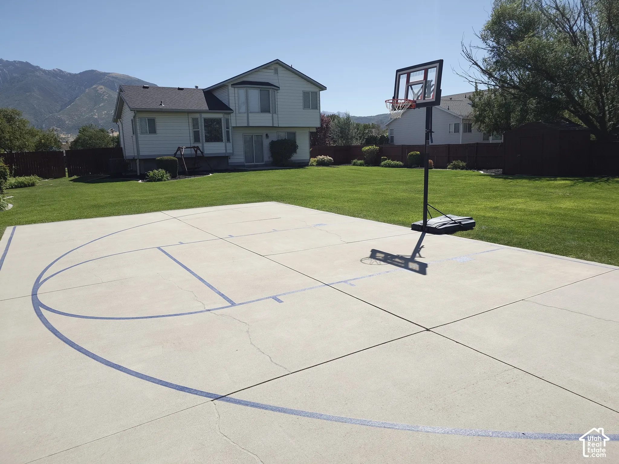 Expansive backyard featuring a concrete sports court, manicured lawn, perimeter wood fencing, and a mountain backdrop