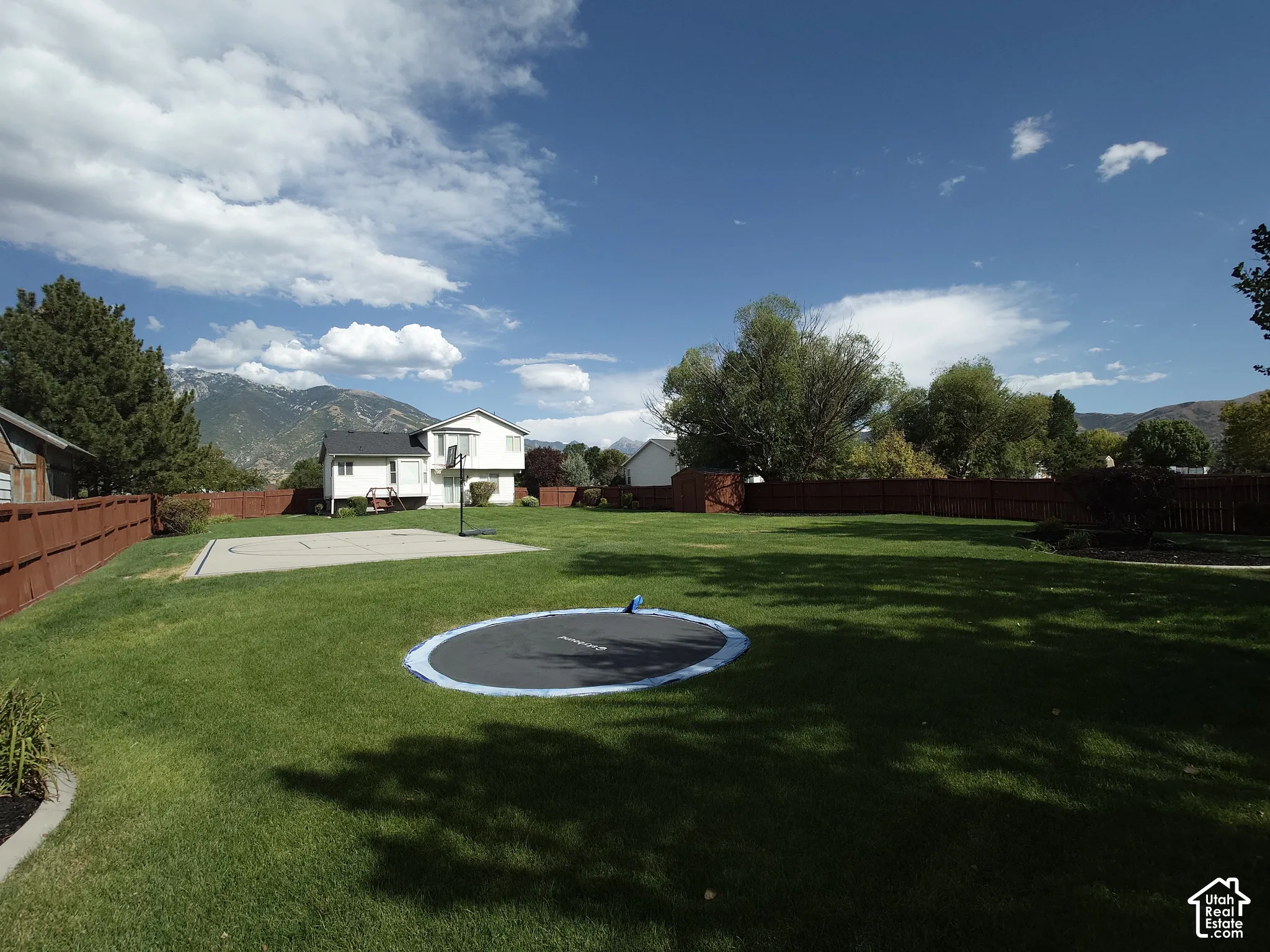 Expansive backyard featuring a grass lawn, perimeter fencing, concrete hardscaping, and mountain backdrop