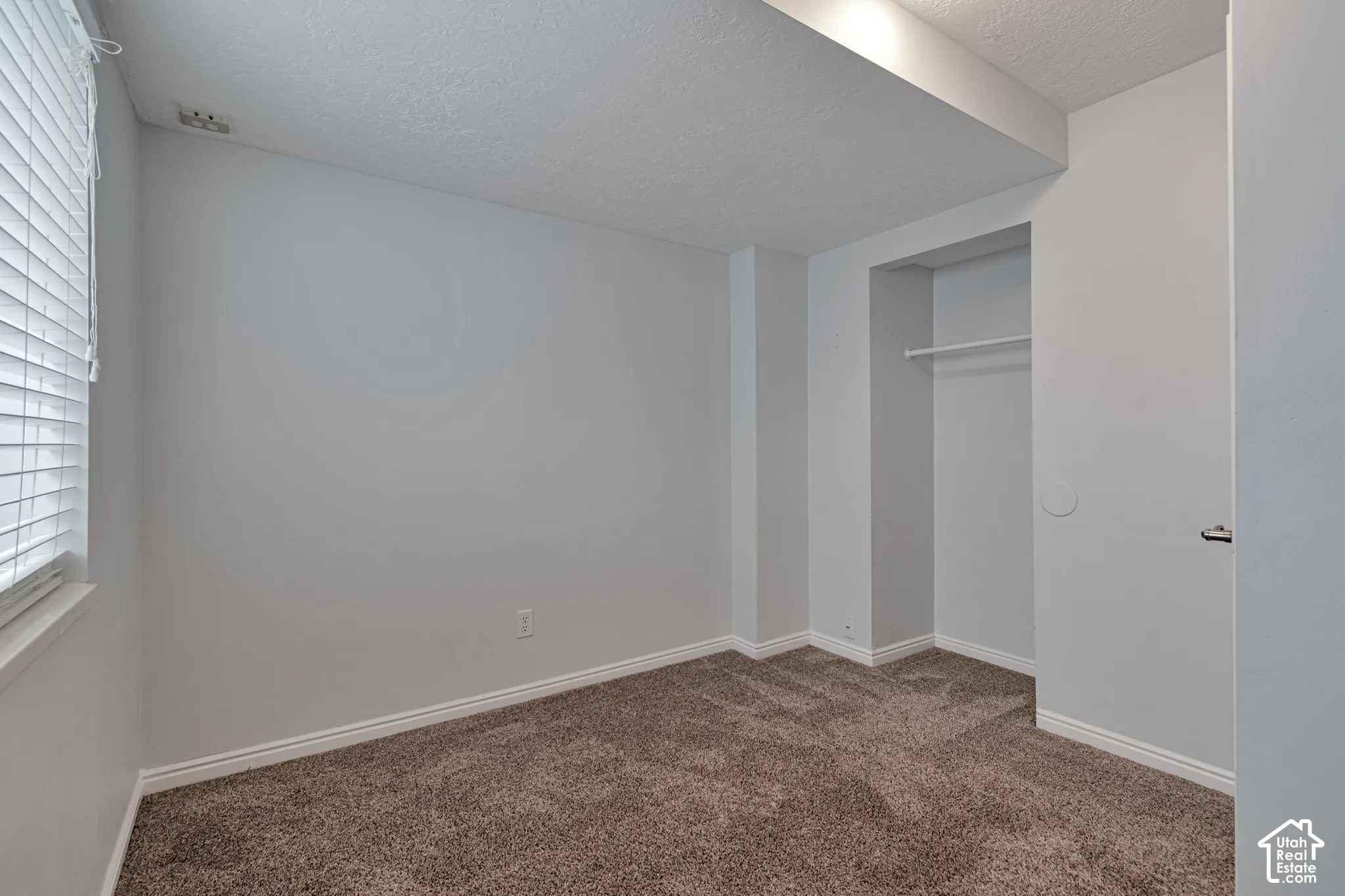 Room featuring neutral wall tones, wall-to-wall carpeting, horizontal window blinds, and a built-in closet with a fixed hanging rod