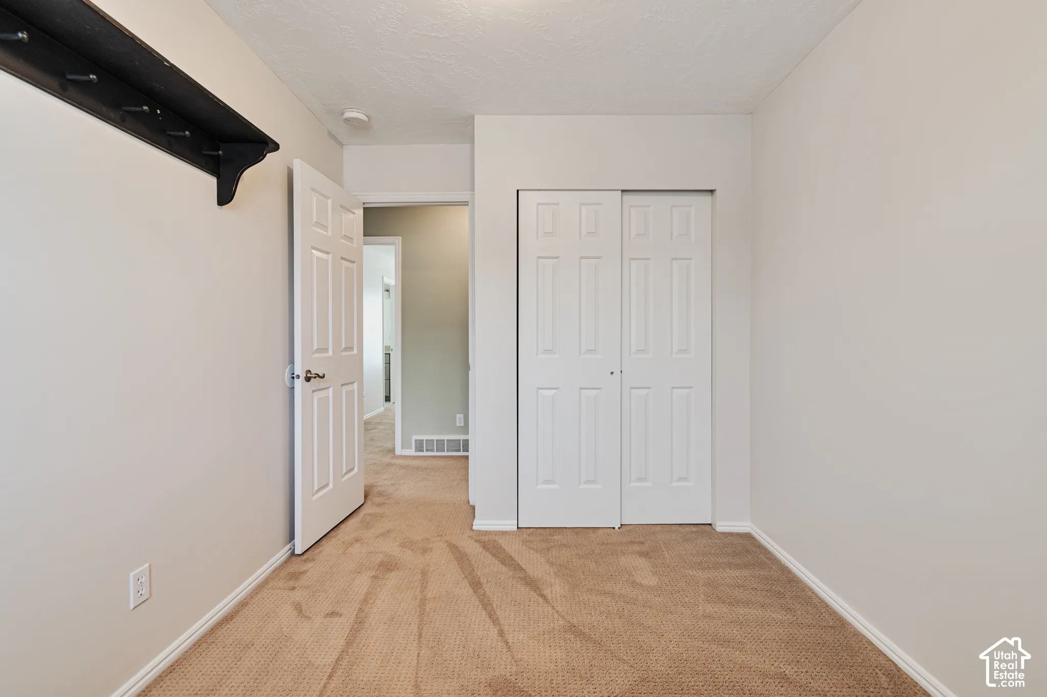 Interior space featuring neutral wall tones, carpeted flooring, a white paneled closet door, and a wall-mounted storage shelf