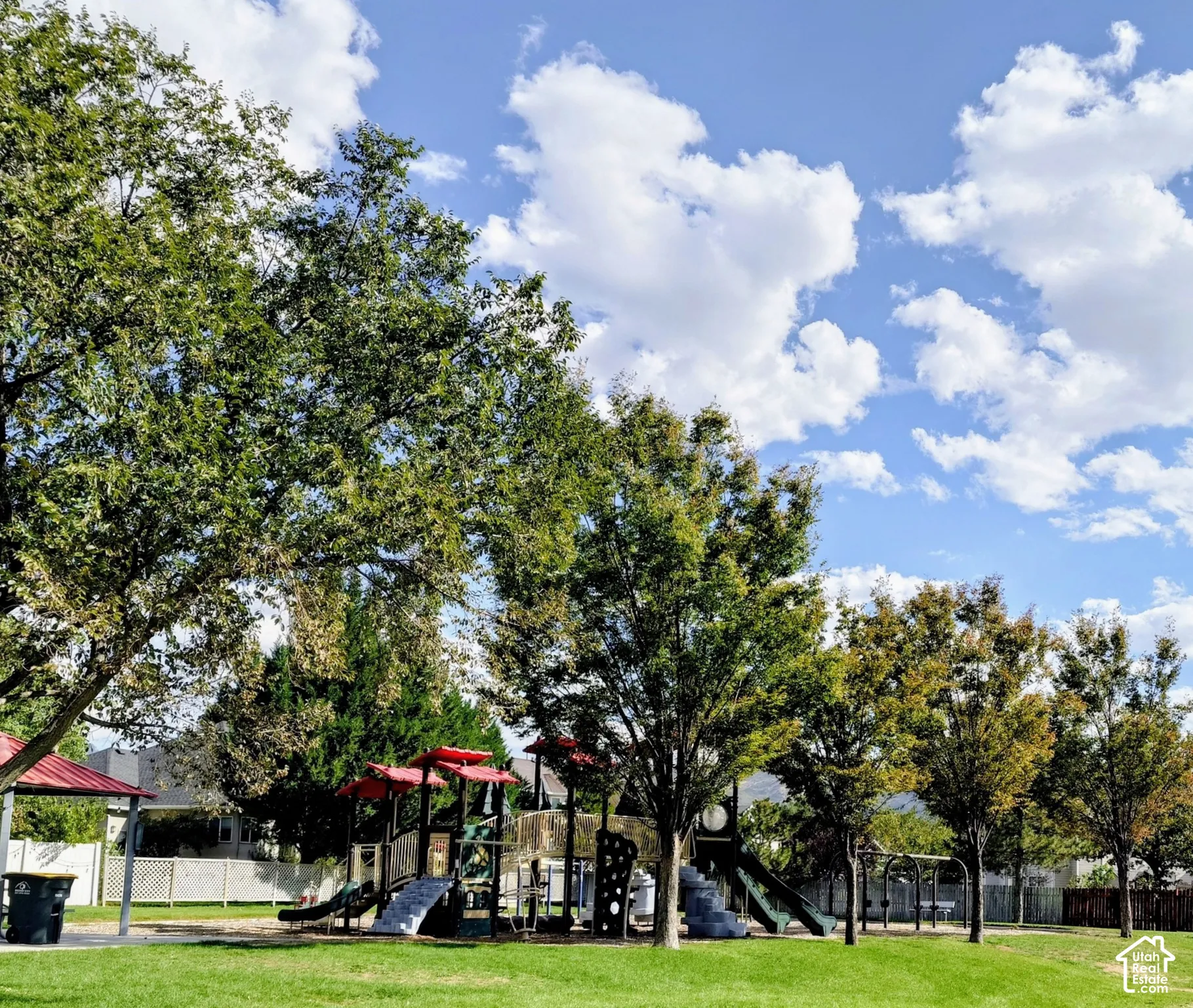 Outdoor recreation area featuring mature trees, expansive lawn, a playground structure, and a covered pavilion