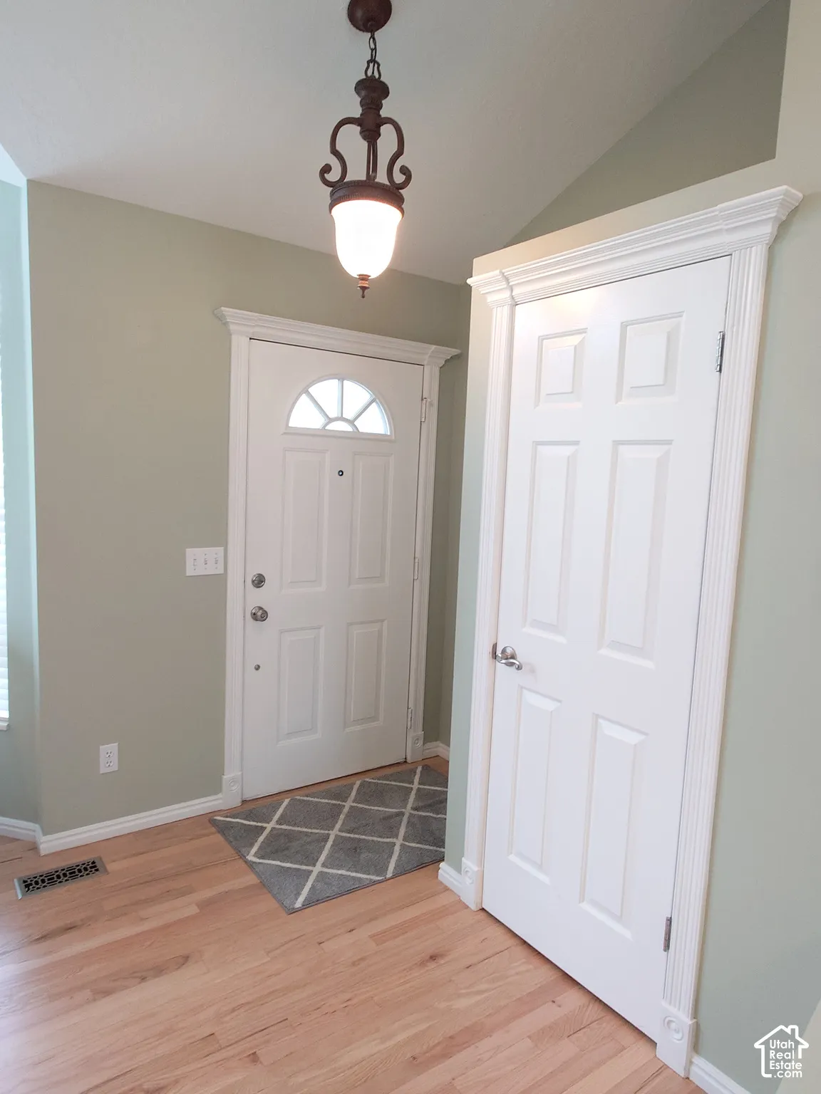 Entryway featuring wood-finish flooring, vaulted ceiling, ornate hanging light fixture, and white six-panel interior door with fluted casing and rosettes