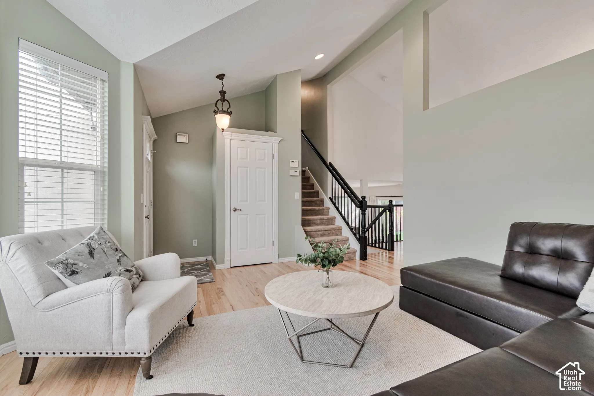 Vaulted ceilings, wood-finish flooring, staircase with a black metal railing, pendant lighting, and neutral wall tones