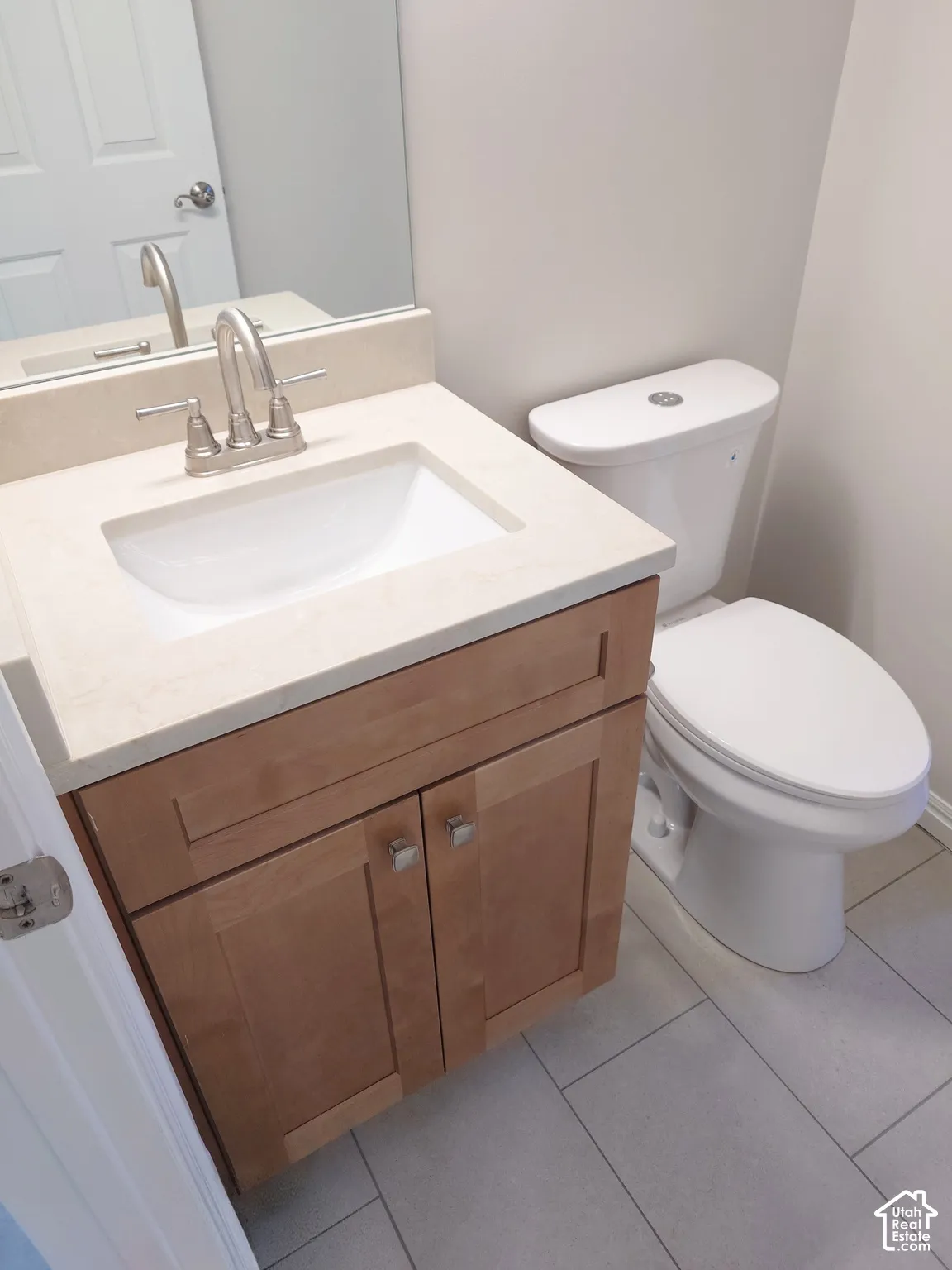 Vanity featuring light wood-finish cabinetry, an integrated stone-composite countertop with an undermount basin, a brushed-nickel widespread faucet, and large-format tile flooring