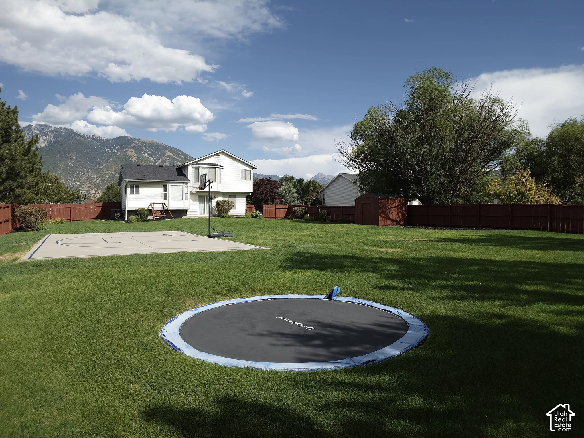 Expansive backyard featuring a concrete sports court, wood-style perimeter fencing, and mountain scenery