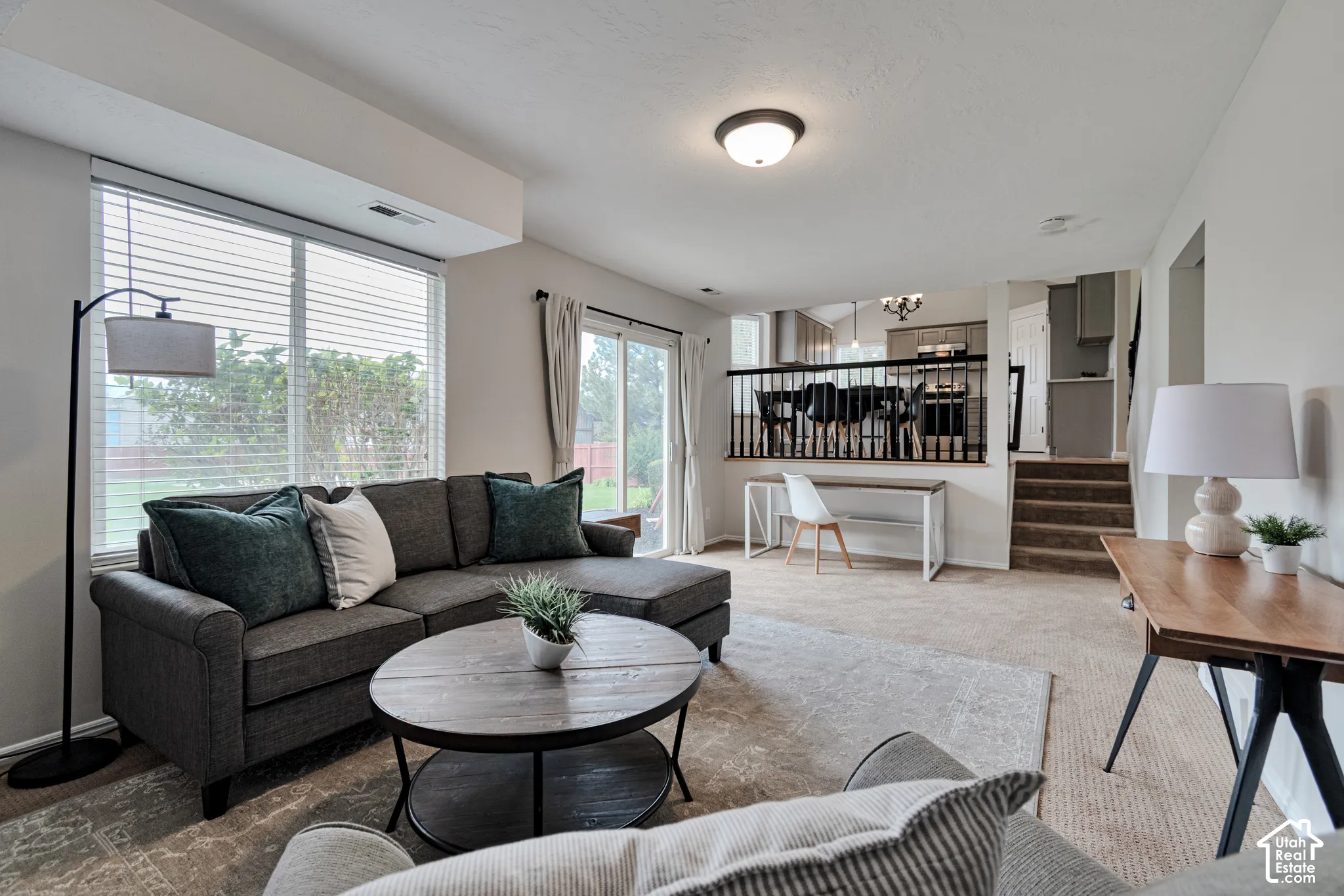 Living area featuring large windows, sliding glass doors, neutral carpeting, and a tiered layout with decorative black metal railing